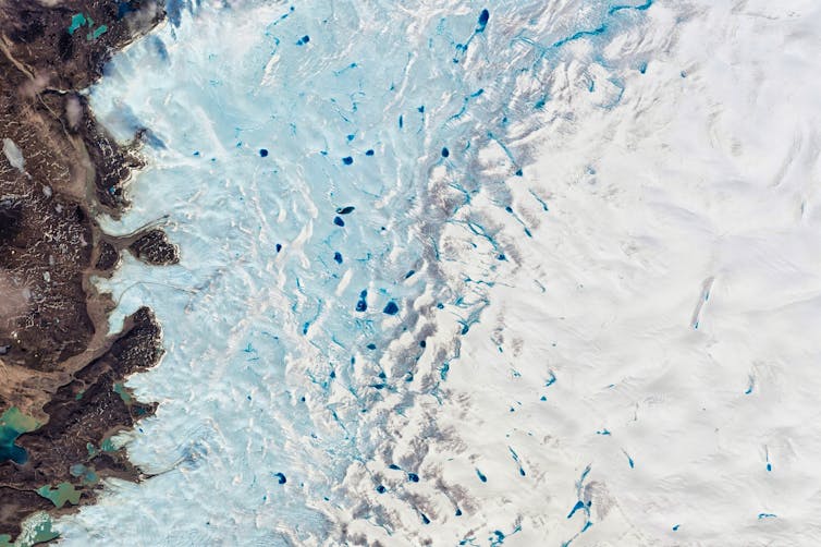 Luftaufnahme einer braunen Klippe, blauem Meer mit weißem Eis und Ozeanberg auf der rechten Seite