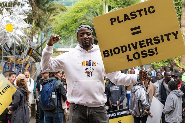Mann hält Schild mit der Aufschrift „Plastik = Verlust der Artenvielfalt“