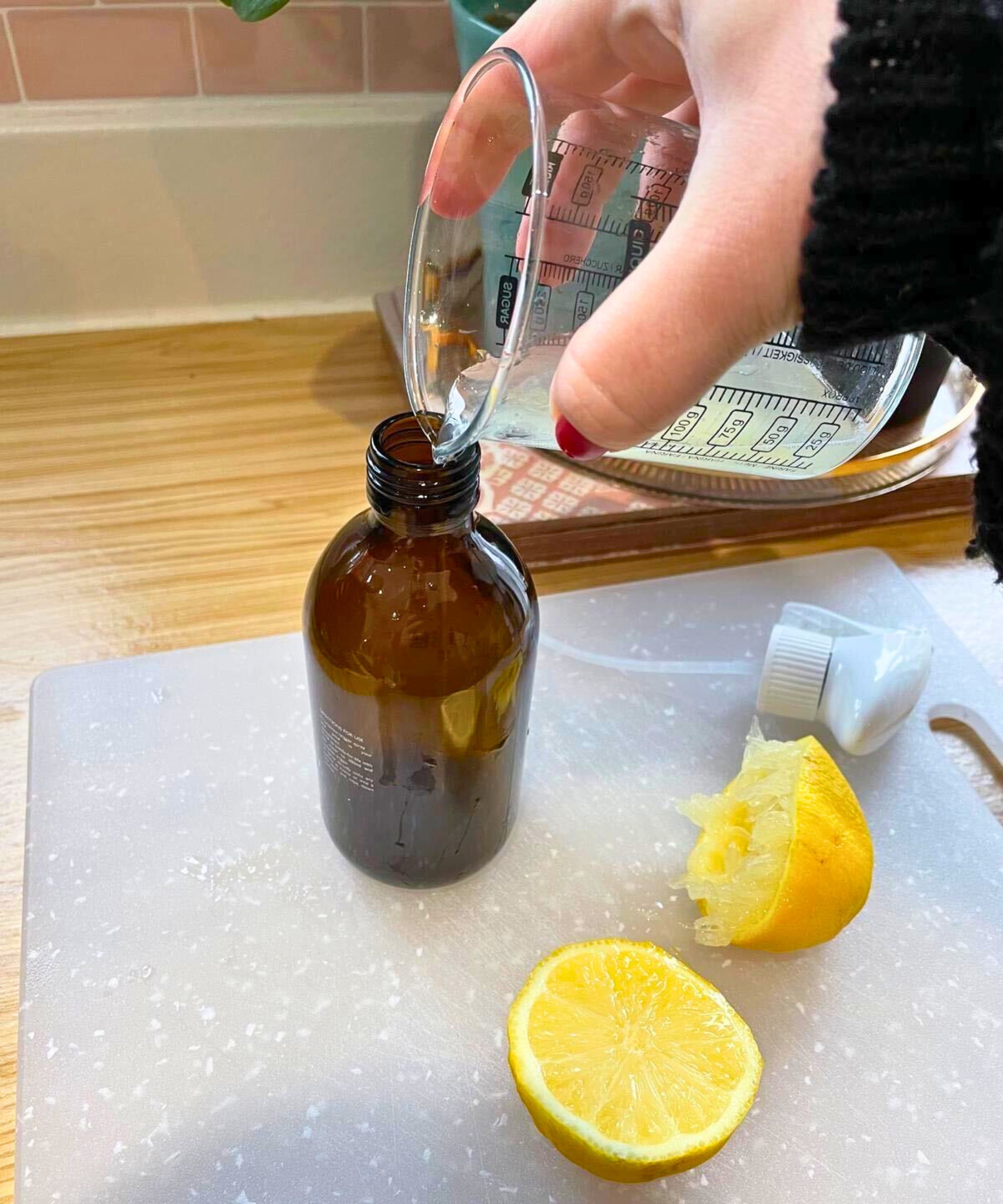Meine Hand gießt Zitronensaft und Wasser in meine bernsteinfarbene Sprühflasche