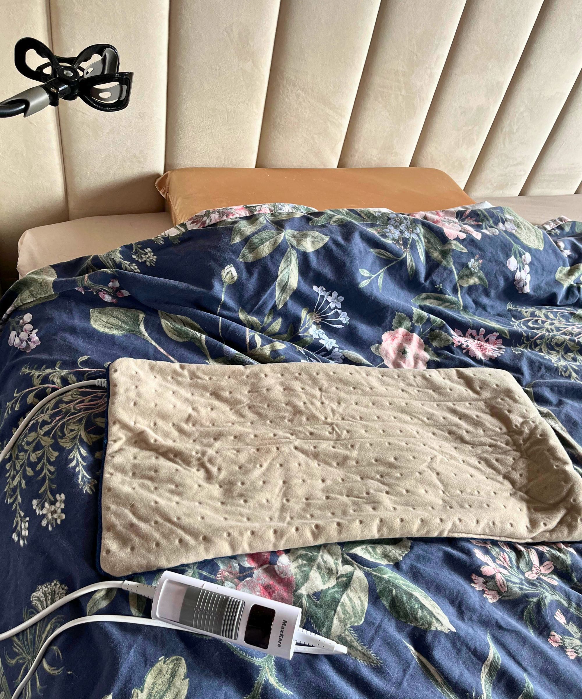 Ein cremefarbenes Heizkissen auf meinem Bett mit dunkelblauer Blumendecke und getäfeltem, gepolstertem, cremefarbenem, hohem Kopfteil