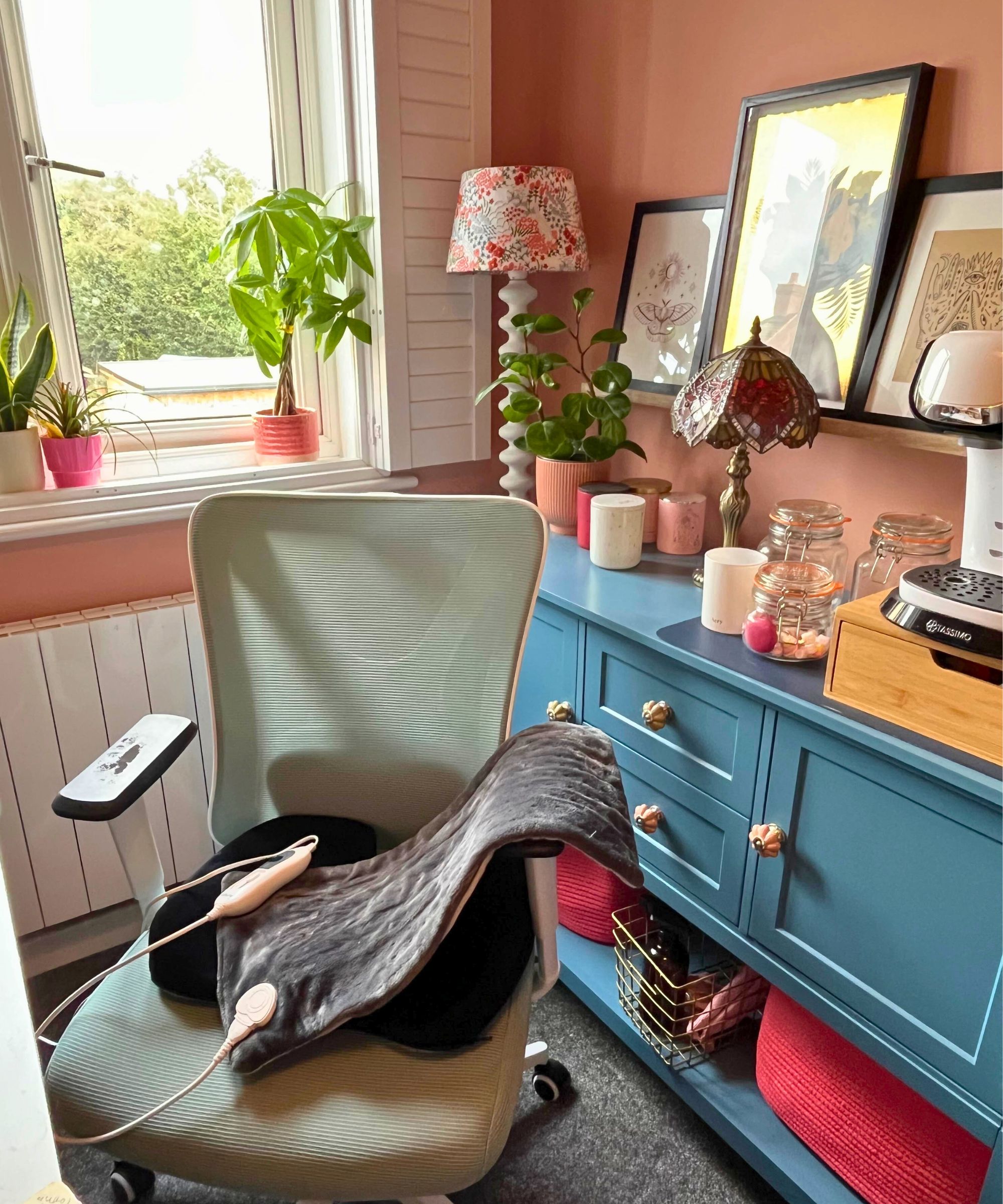 Mein graues Heizkissen auf meinem hellgrünen Mesh-Bürostuhl in einem terrakottafarbenen Arbeitszimmer mit blauer Sideboard-Bobby-Lampe und weißen Fensterläden im Hintergrund