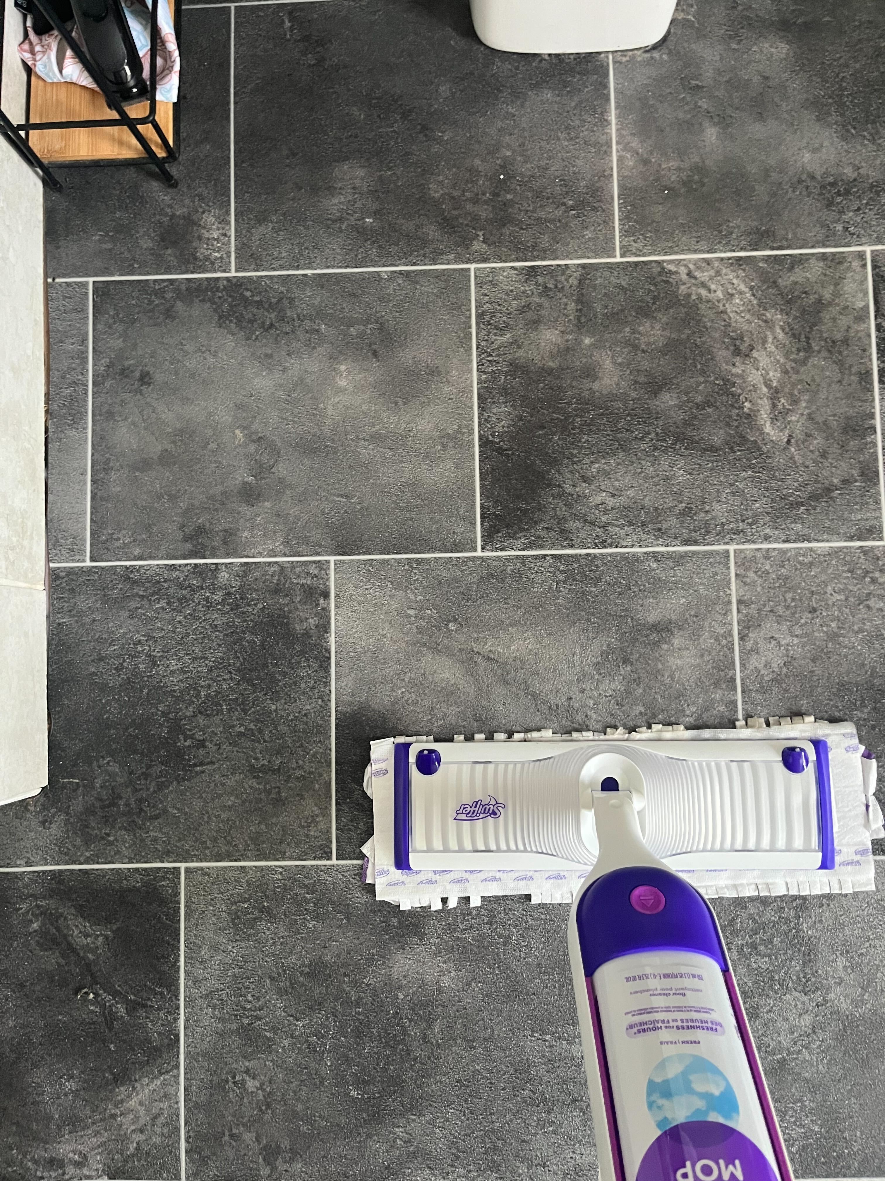 Verwendung eines lila-weißen Swiffer-Wischmopps zum Reinigen eines Badezimmerbodens