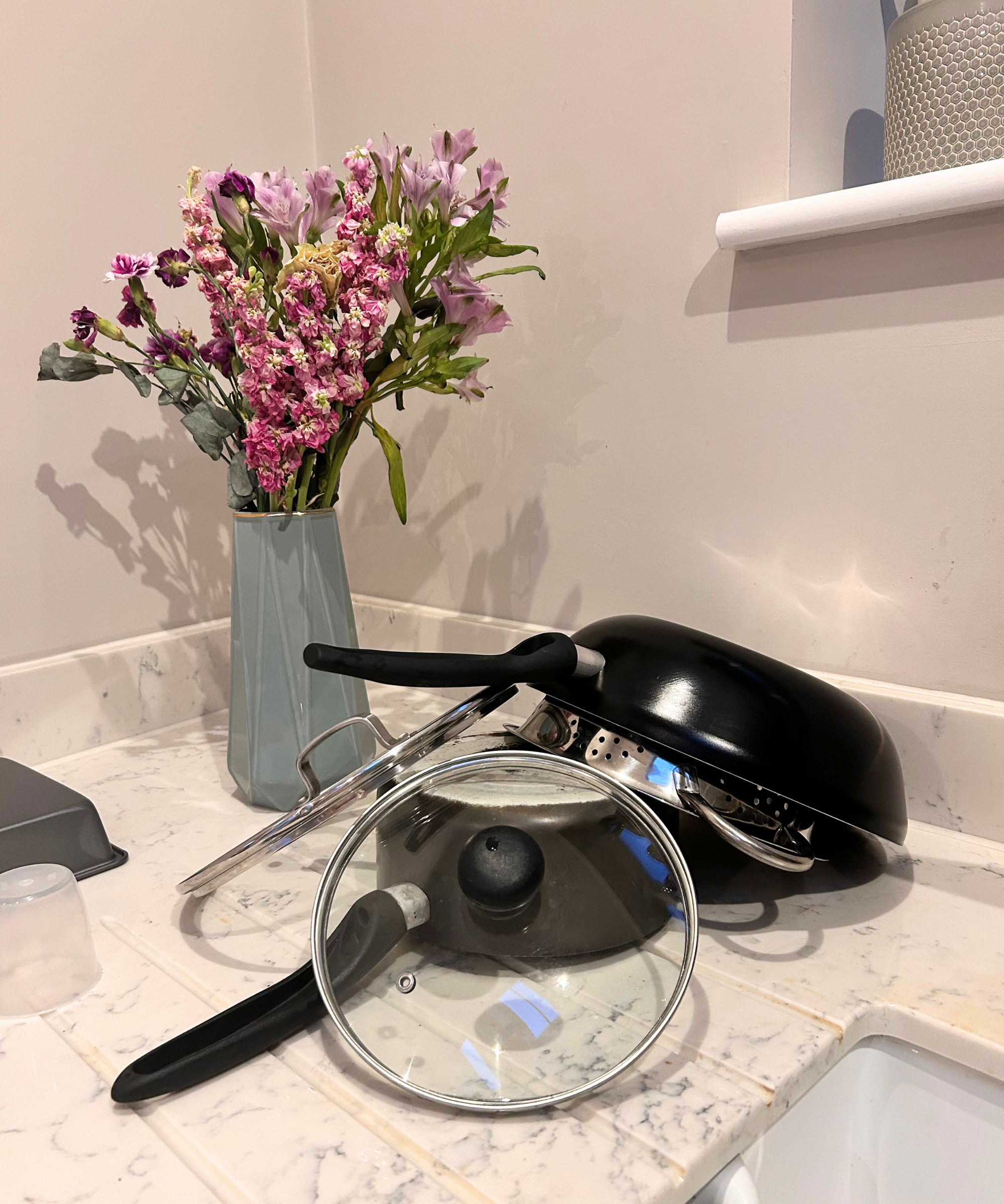 Vorher: Töpfe und Pfannen stehen zum Trocknen auf der Küchenarbeitsplatte mit Blumen in einer Vase.