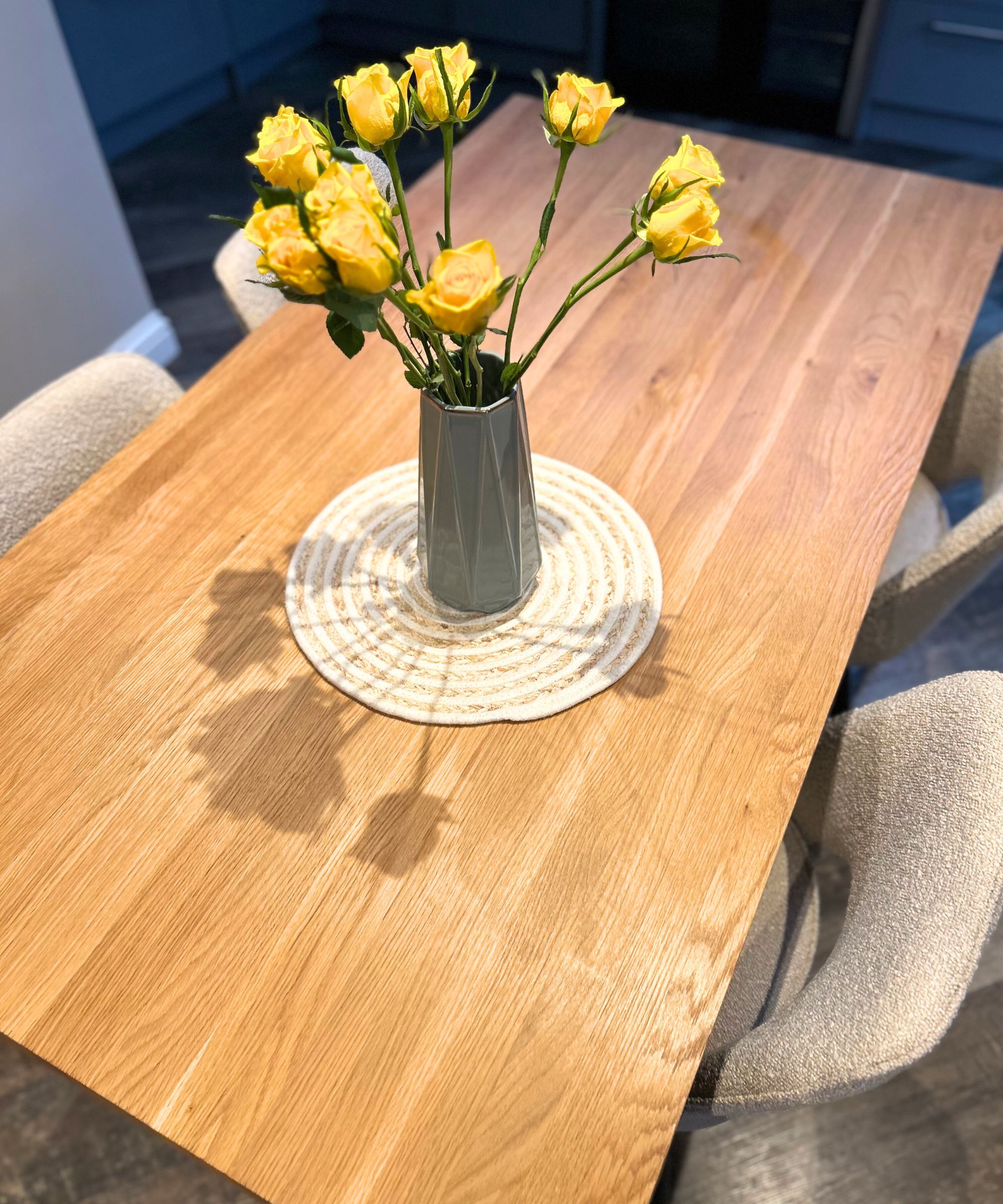 Esstisch aus Holz mit Bouclé-Stühlen und gelben Rosen in der Mitte in einer grünen Vase