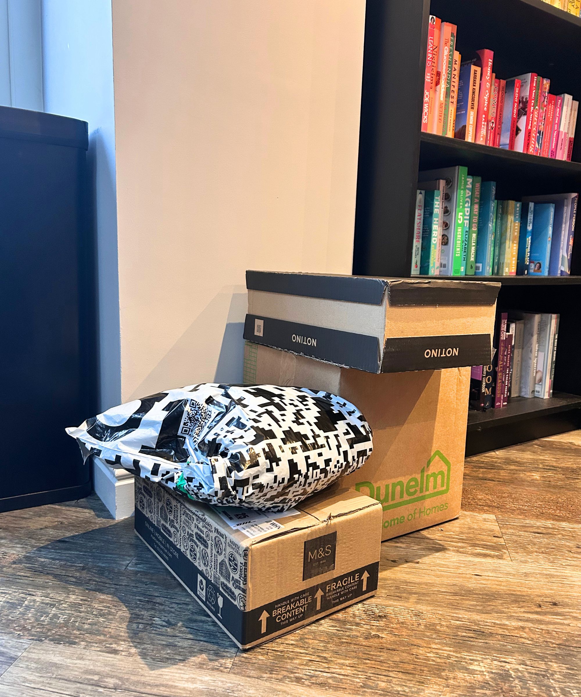 Stapel verpackter Gegenstände auf dem Boden neben einem farblich abgestimmten Bücherregal