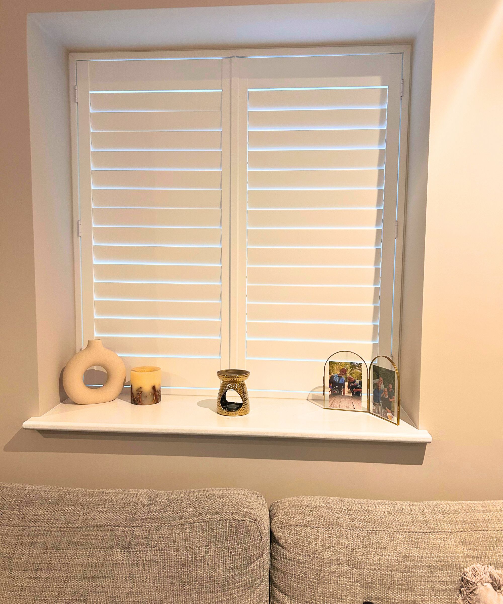 Ein ordentliches Wohnzimmer mit weißen Fensterläden, Kerzen, Ölbrenner und Goldrahmen