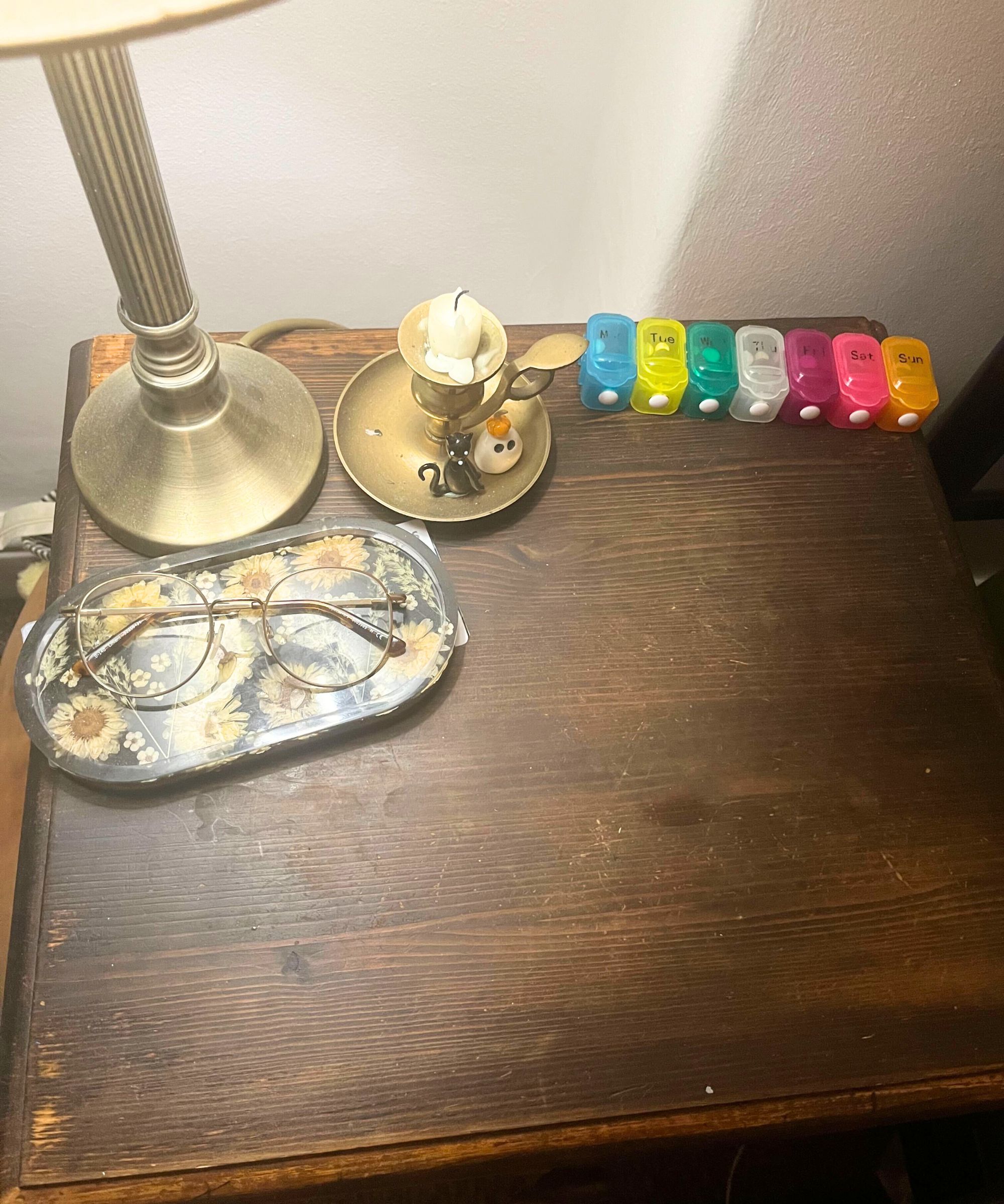 Die Oberseite eines dunklen Nachttischs mit einer Lampe, einer Brille, einer Pille -Schachtel und einem Kerzenhalter