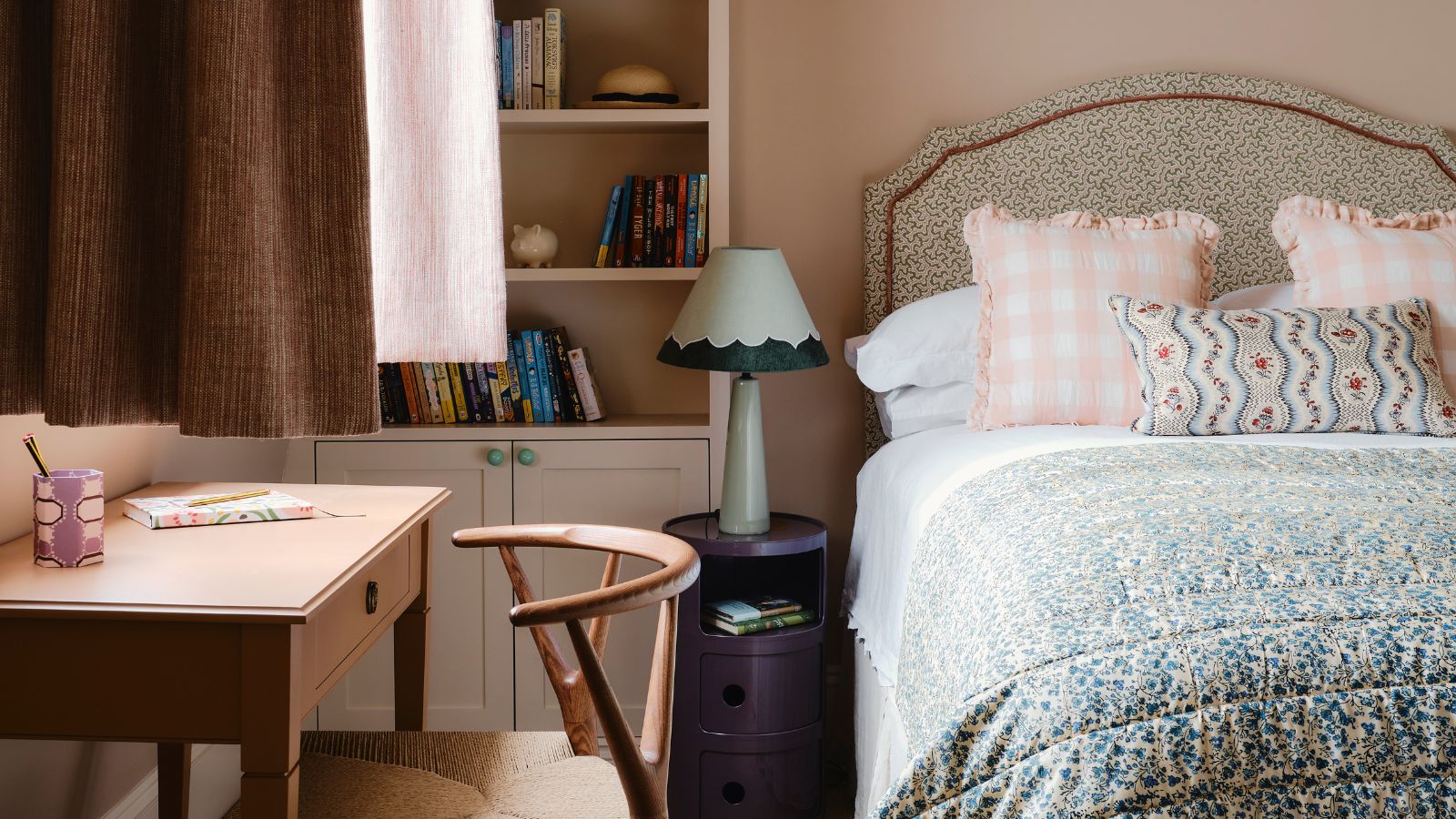 pink bedroom with built in bookshelf and an upholstered patterned bed styled with white linens, pink gingham pillows, a floral lumbar pillow and a ditsy floral throw