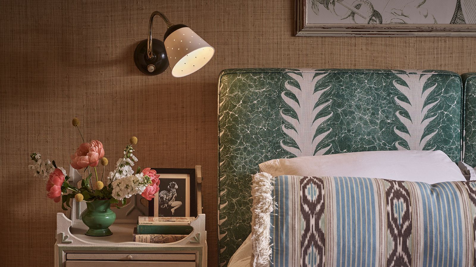 A bedroom with a blue patterned headboard, a wall mounted bedside lamp, and painted nightstand.