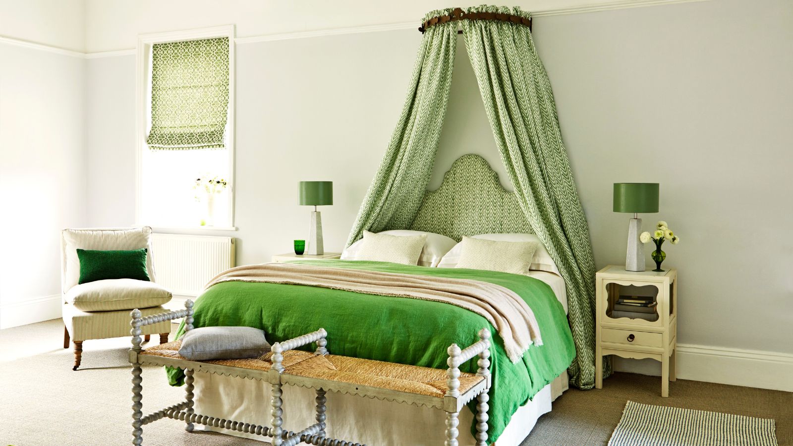 Bedroom, green theme, corona with herrigbone fabric and matching headboard in white wall with armchair, bedside tables, green lamps, rugs and small table at the foot of the bed.