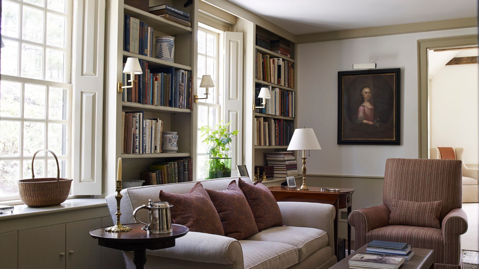Traditional living room with sconces, large windows and sofa with bookshelves and antique painting