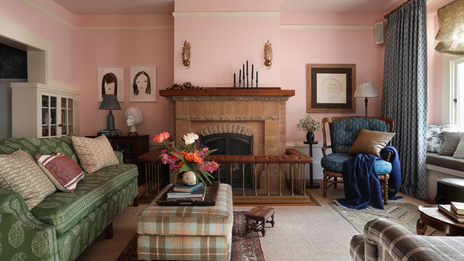 traditional cozy living room with pink walls, green sofa, brick fireplace, and plaid ottoman