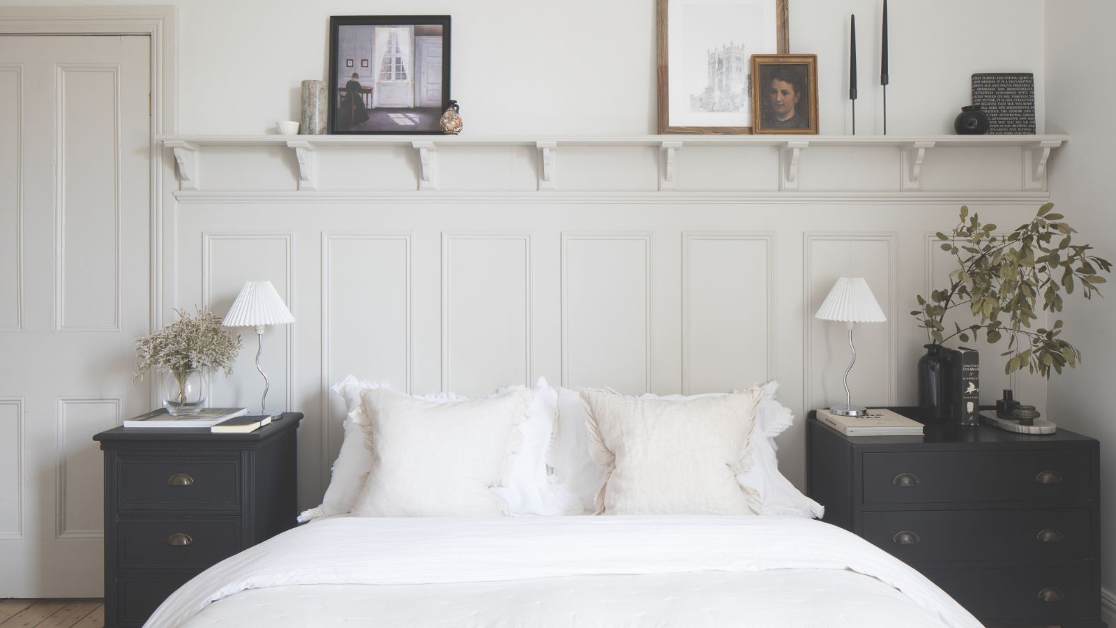 Ein weißes Schlafzimmer mit einem Doppelbett und sentimentalen Gegenständen, die auf einem Regal über dem Bett ausgestellt sind