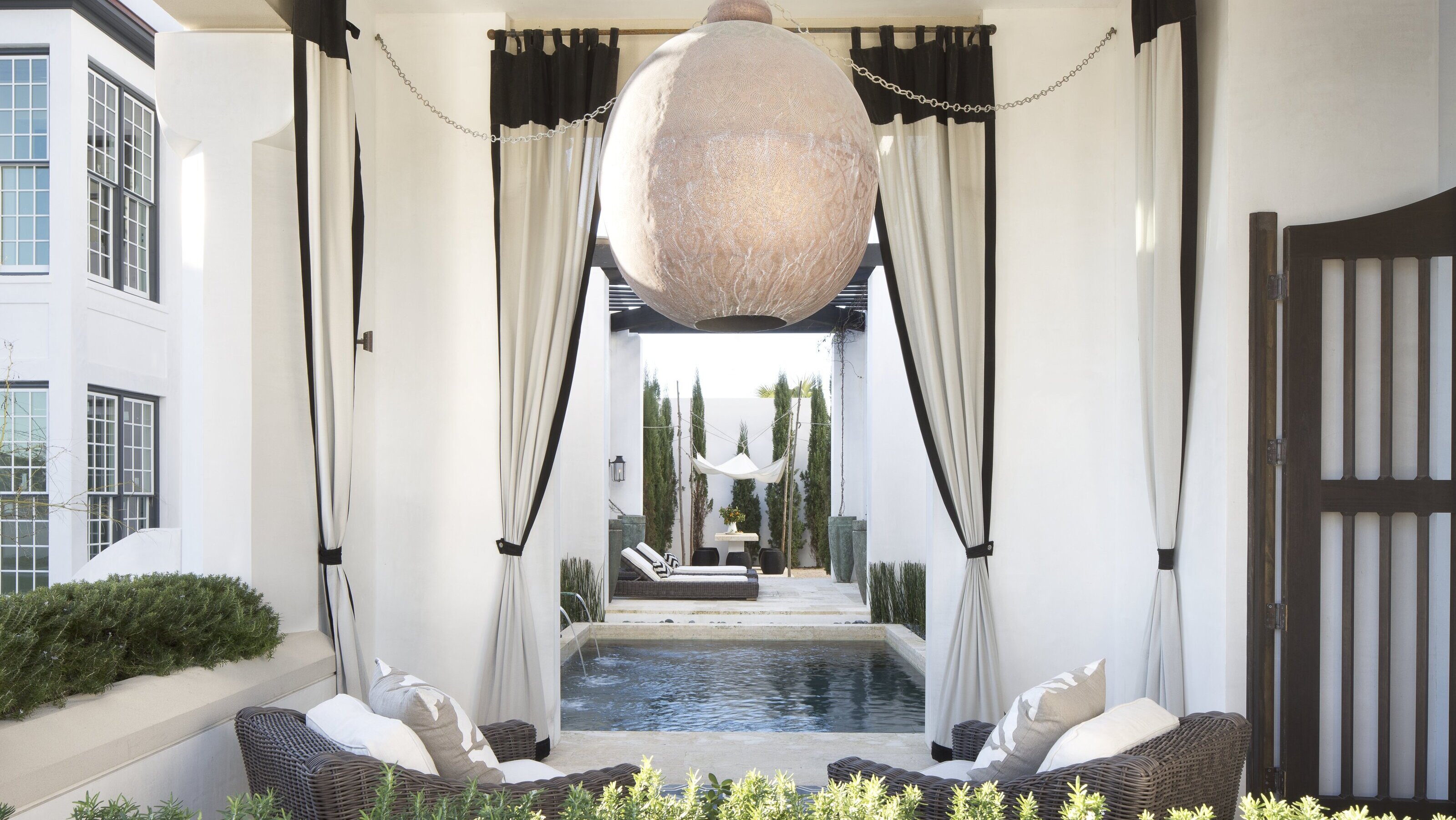Ein geschützter Außenbereich mit kugelförmigen Lampenschirm, Gartenmöbeln und Vorhängen mit schwarzer Ausstattung 
