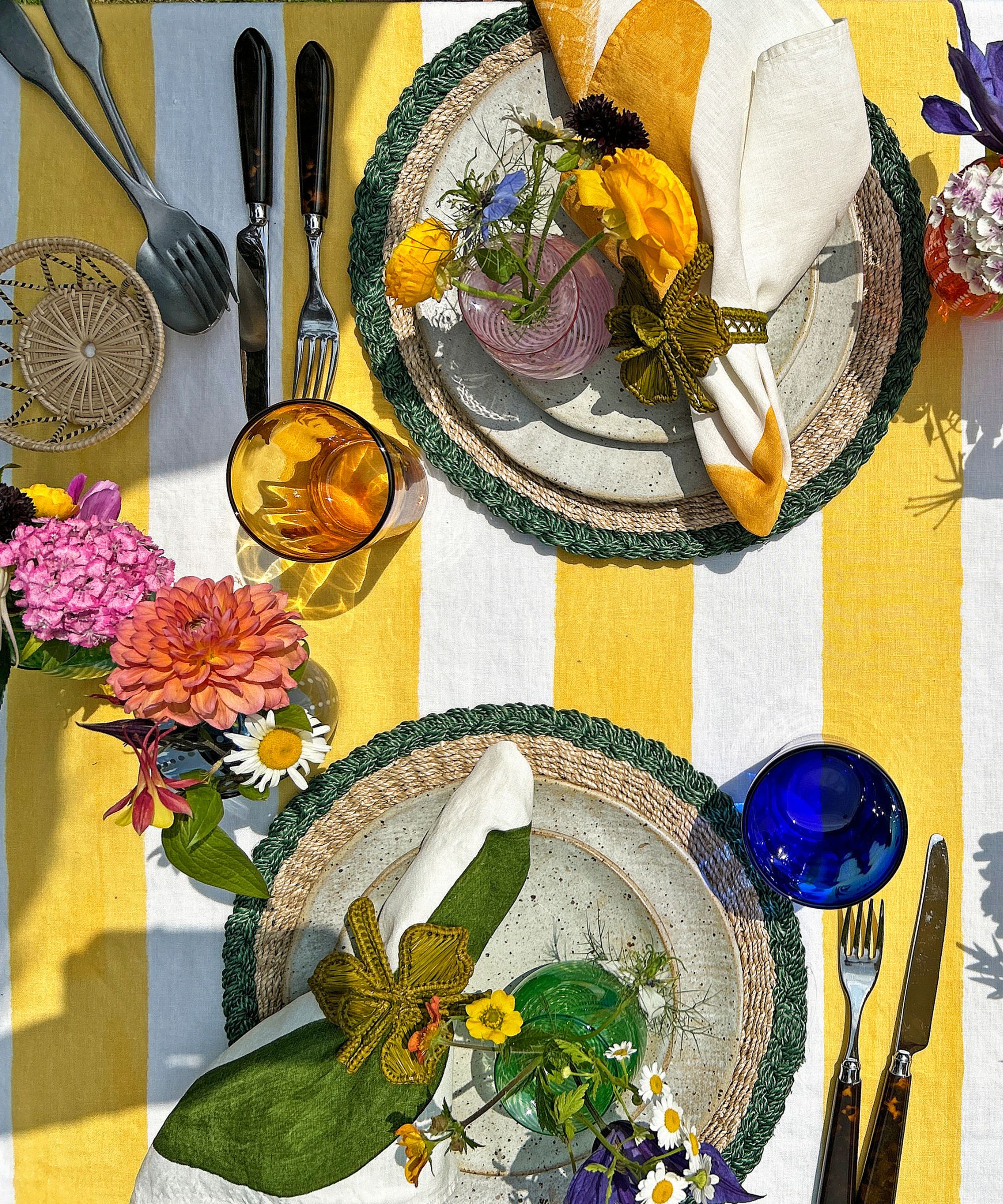 Gelbe und weiße Streifen -Tischdecke mit Tellern, Servietten und farbigen Brillen, die darauf eingestellt sind, mit Blumenvasen