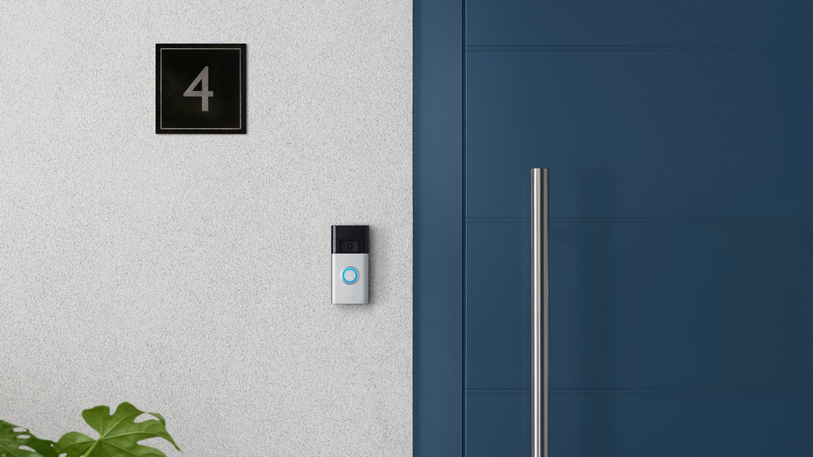 Eine Ring-Kamera-Türklingel der zweiten Generation an einer weißen Wand neben einer blauen Haustür und A ' Nummer 4 ' Platte. 