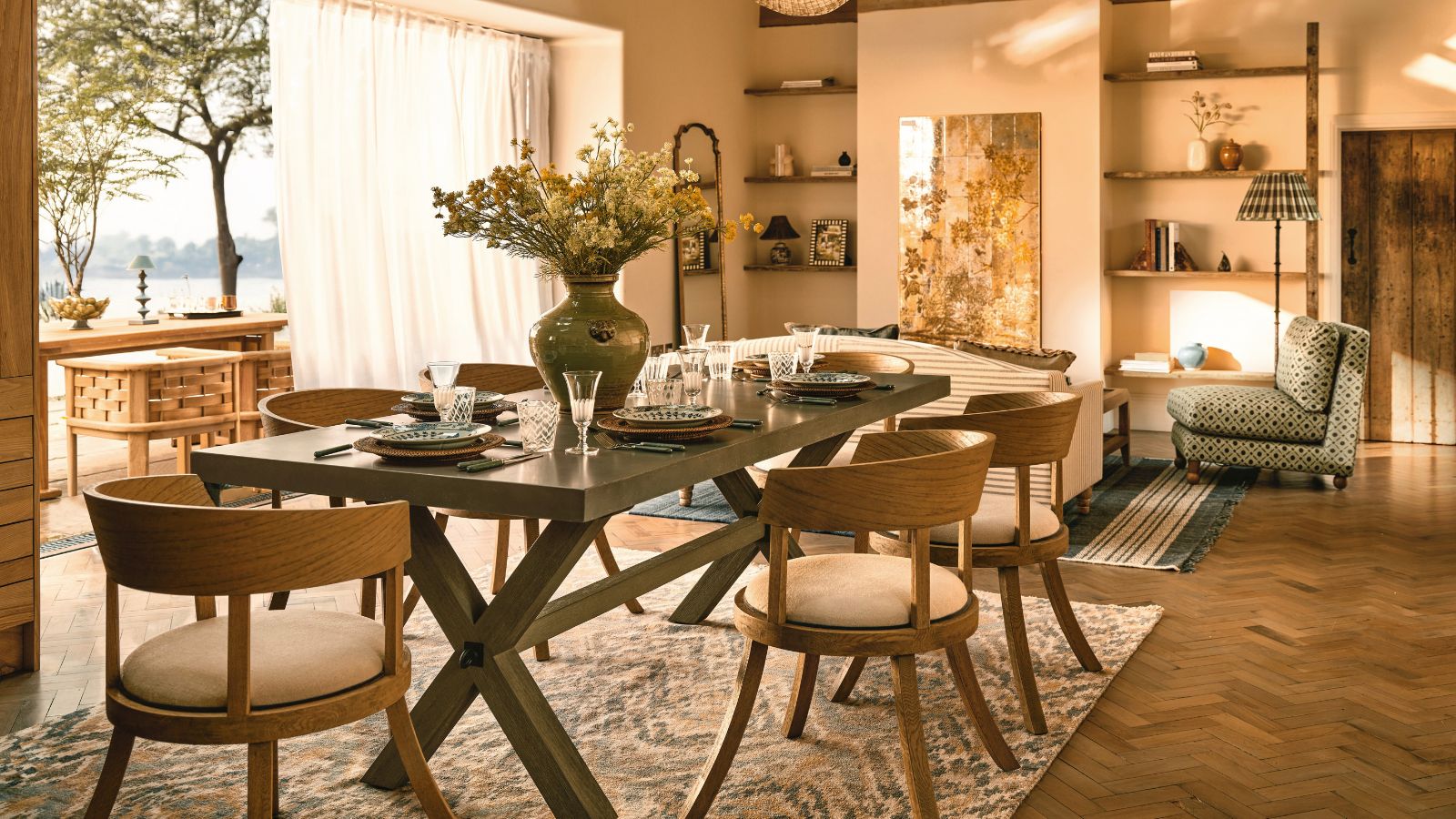 Ein warmes Wohnzimmer mit einem großen schwarzen Tisch mit sechs Stühlen. Eine große zweifaltende Tür hinter dem Tisch, die sich auf einer sonnigen Terrasse öffnet. 