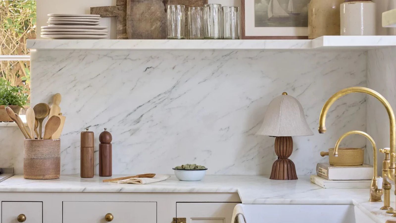 Eine Küche mit warmen neutralen Schränken und einer Marmor -Arbeitsplatte, Backsplash und Regal, die mit kuratiertem Dekor aus dem Innenraum von Shoppe Bamern dekoriert wurden 
