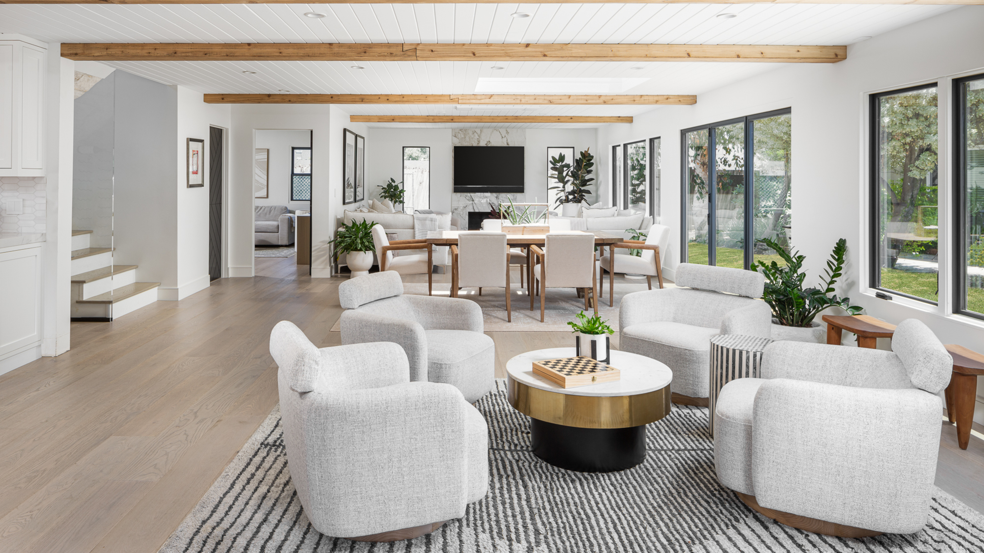 Ein großer offener Wohnraum mit neutraler Farbpalette, weiße Armstühle um einen Couchtisch im Vordergrund und einen Essraum im Hintergrund