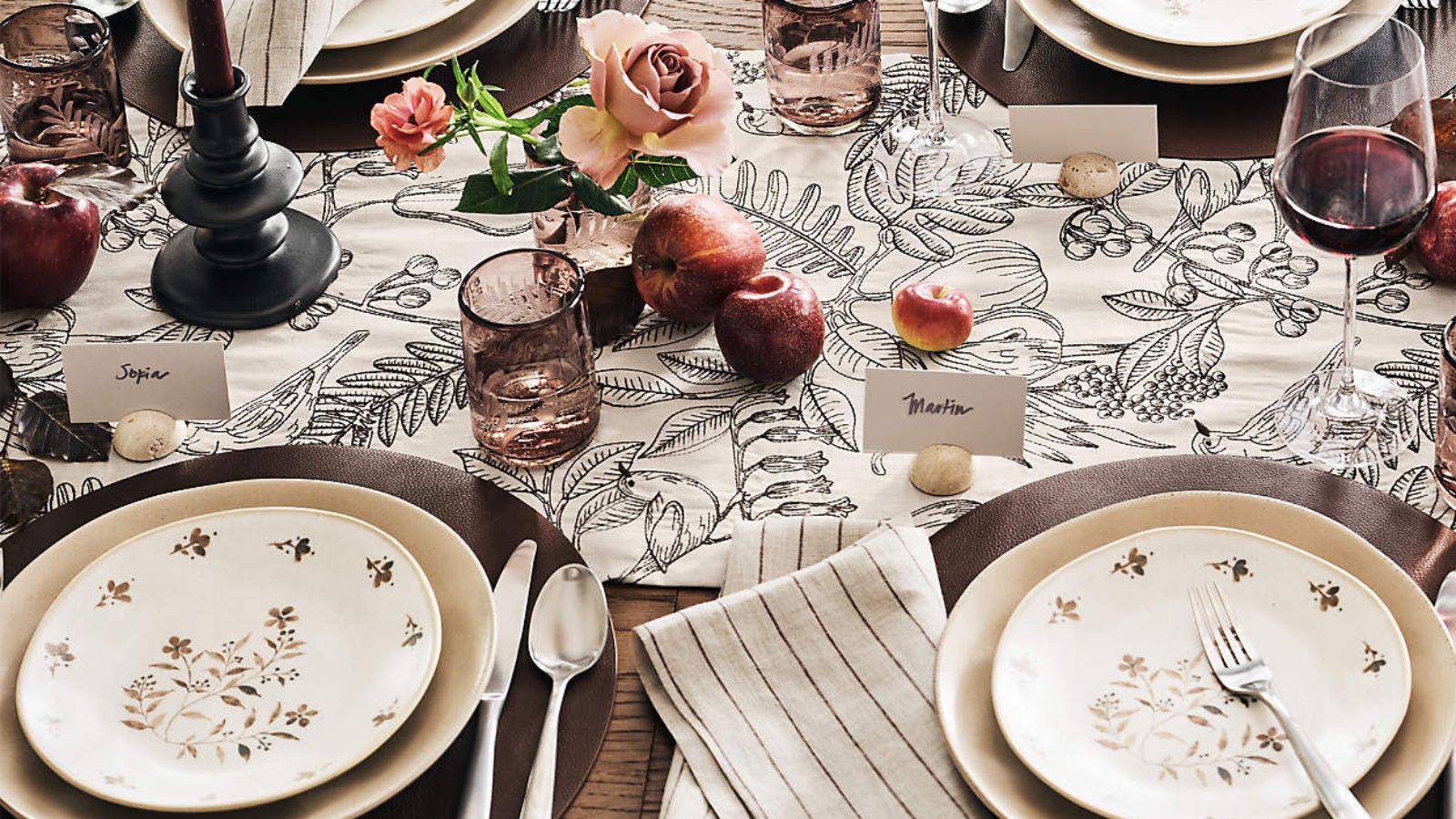 Fall table with cream floral plates, black and white floral runner, and a centerpiece of roses and apples