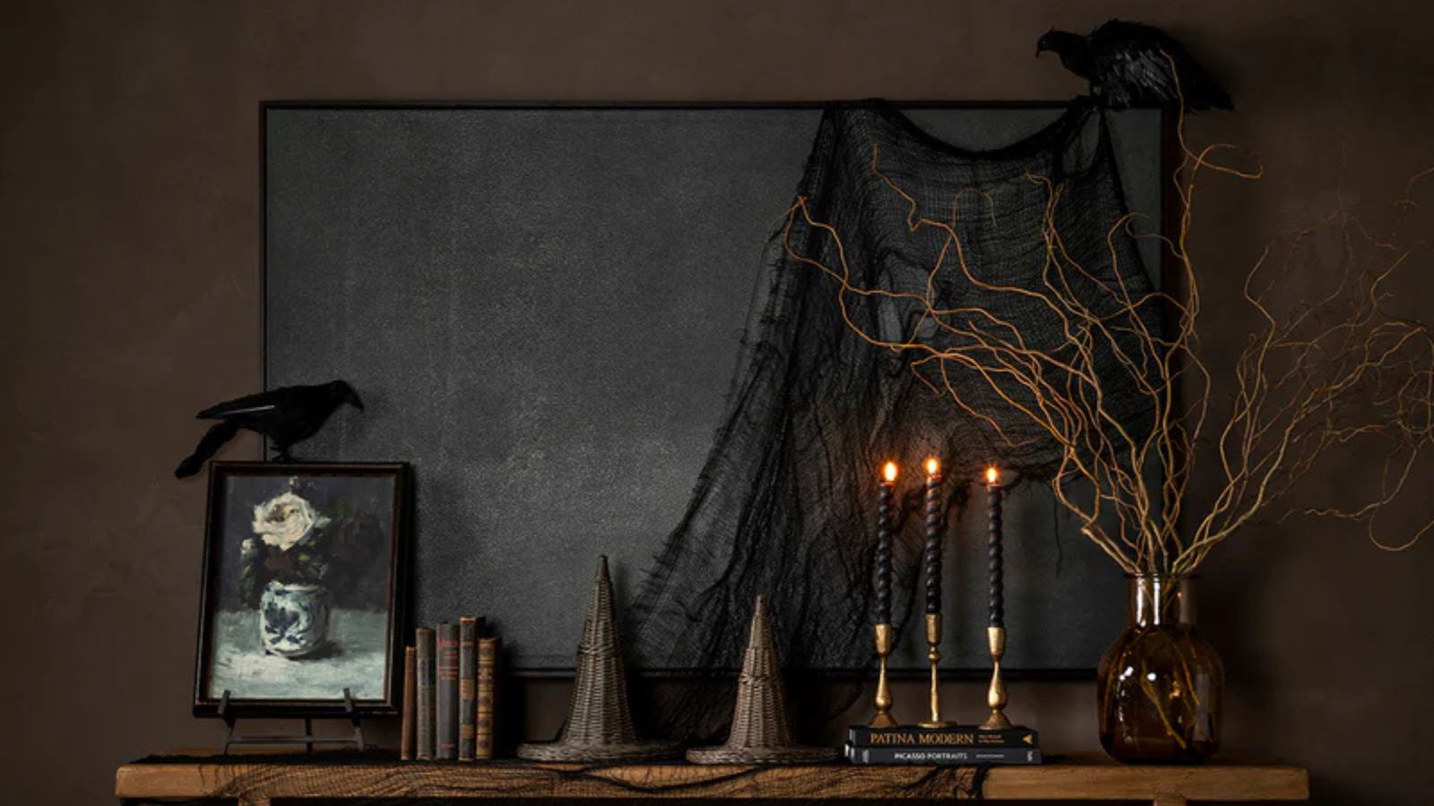 Wooden sideboard with wicker witch hats, black tapered candlesticks, Gothic paintings, and a vase full of twisted branches
