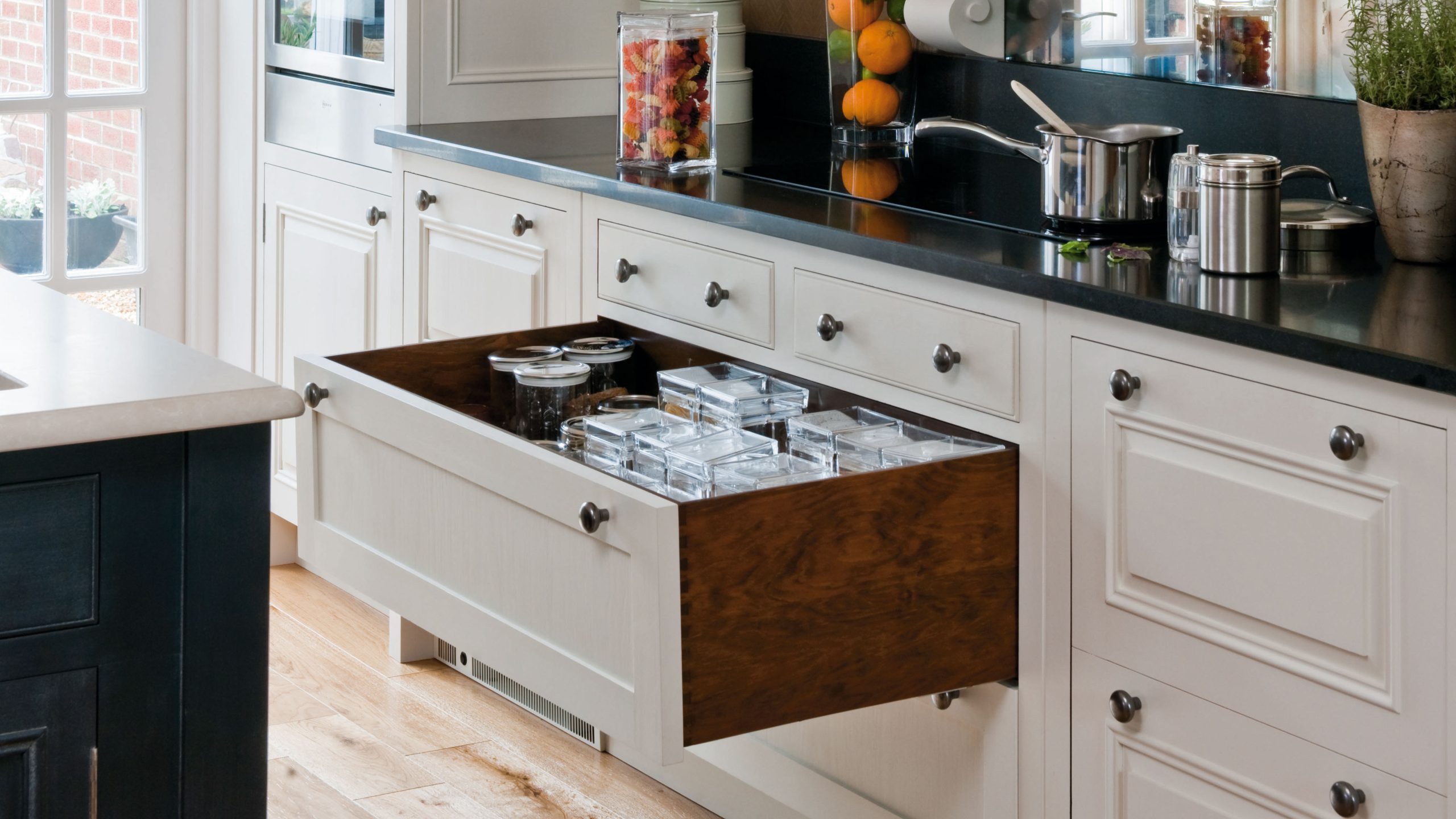 White open plan kitchen, antique style fitted units, black granite worktops, chimney breast mantel, mirrored splashback, open storage drawer, storing dried food in glass jar containers