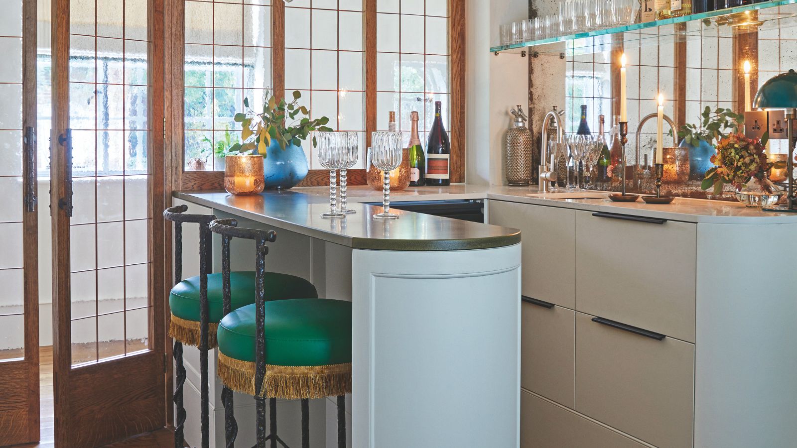 Corner home bar with a peninsular layout, pale blue cabinets, dark stone top, green vintage bar stool and open shelving for drinks and glasses