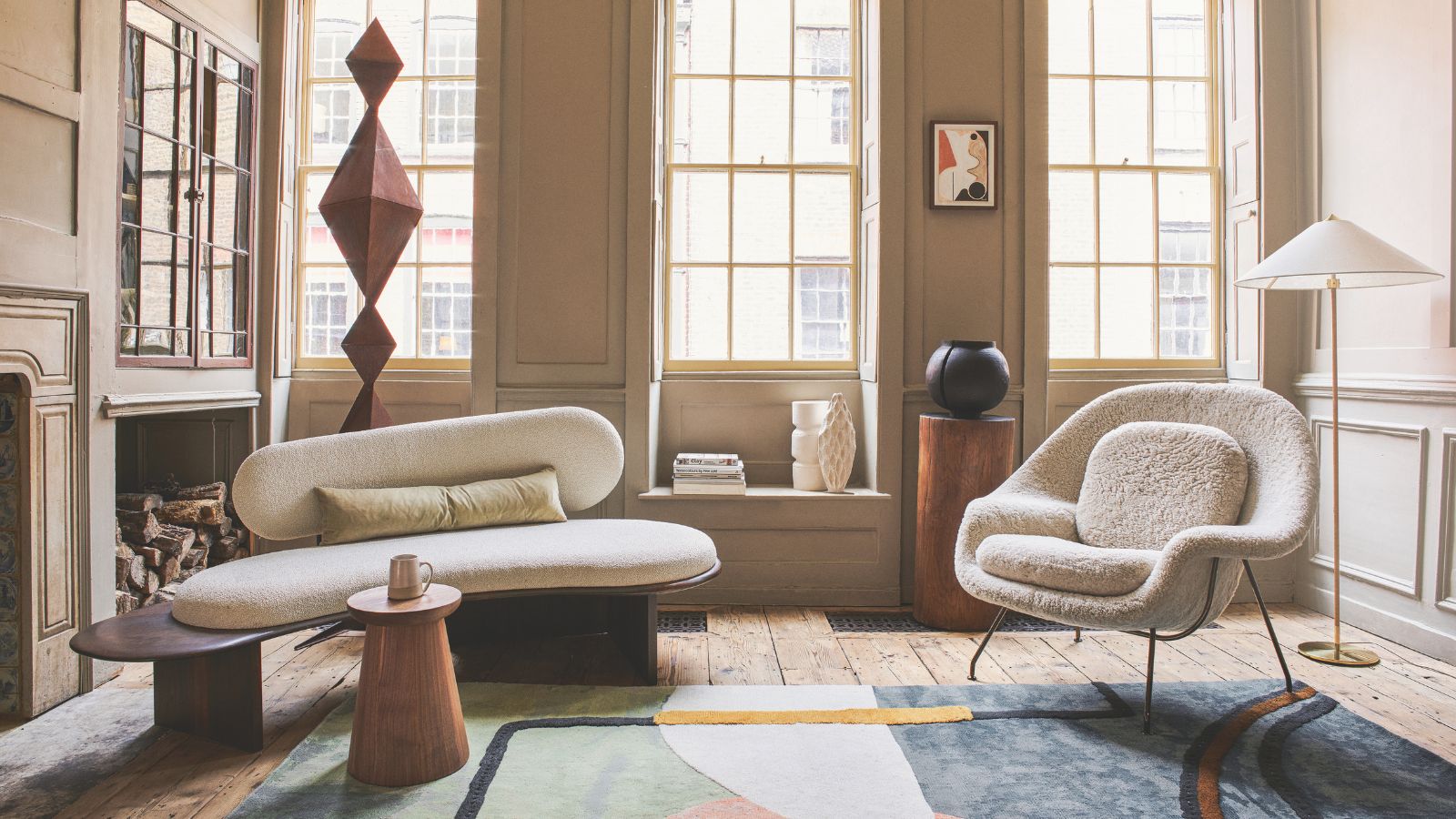City apartment decorated in neutral bright creams, with tall crittal windows and geometric rug. There is a sofa and armchair in cream boucle, with wooden accent pieces