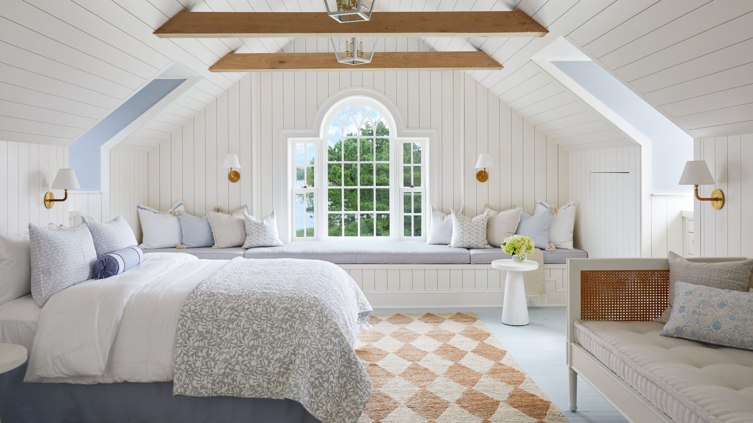 Eastcoastal bedroom featuring a cream-and-white diamond pattern jute area rug, patterned bedding, a high thatched ceiling with exposed wood planks, and a window daybed on the far side of the room
