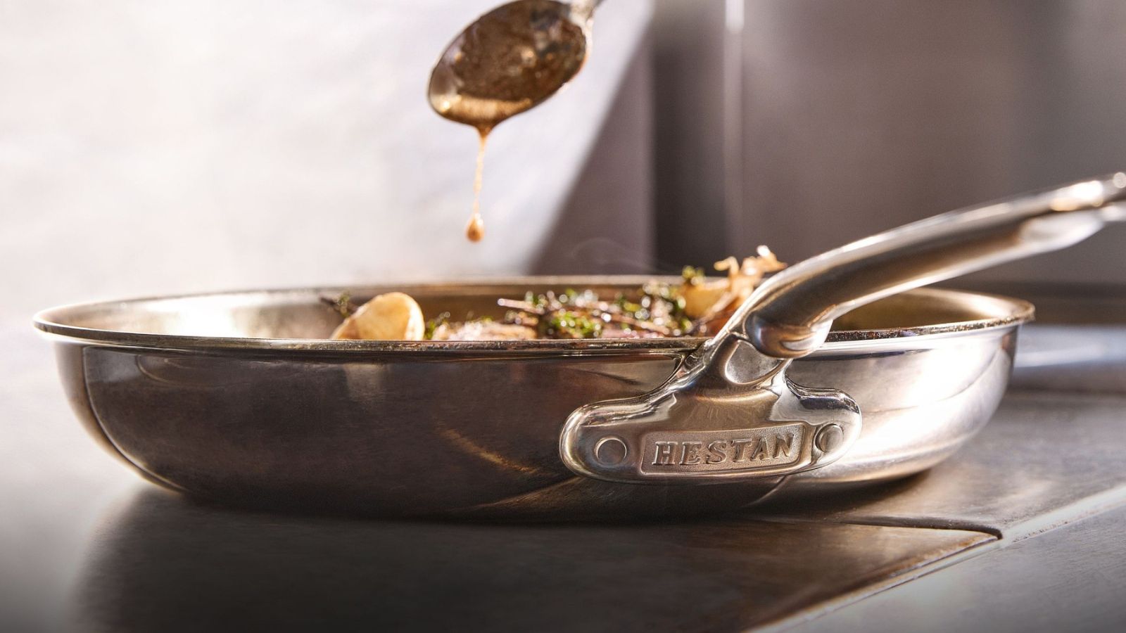 A shot of the logo on the Hestan ProBond Luxe Professional Clad Stainless-Steel Skillet, while basting a steak