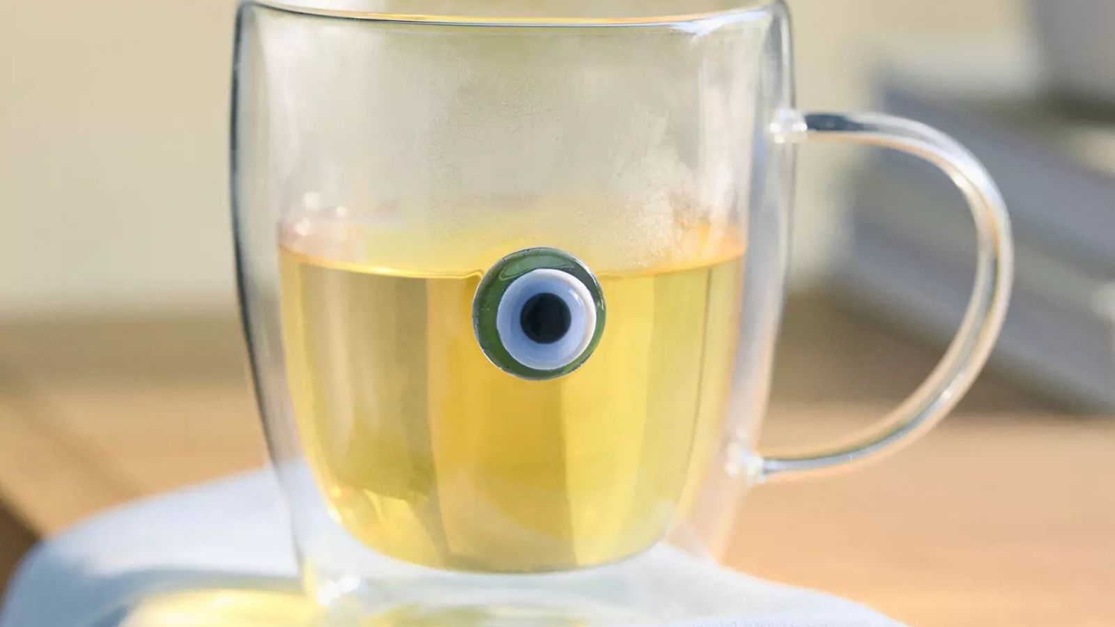 Glass mug with small evil eye design, on a wooden table with a pale blue dish towel