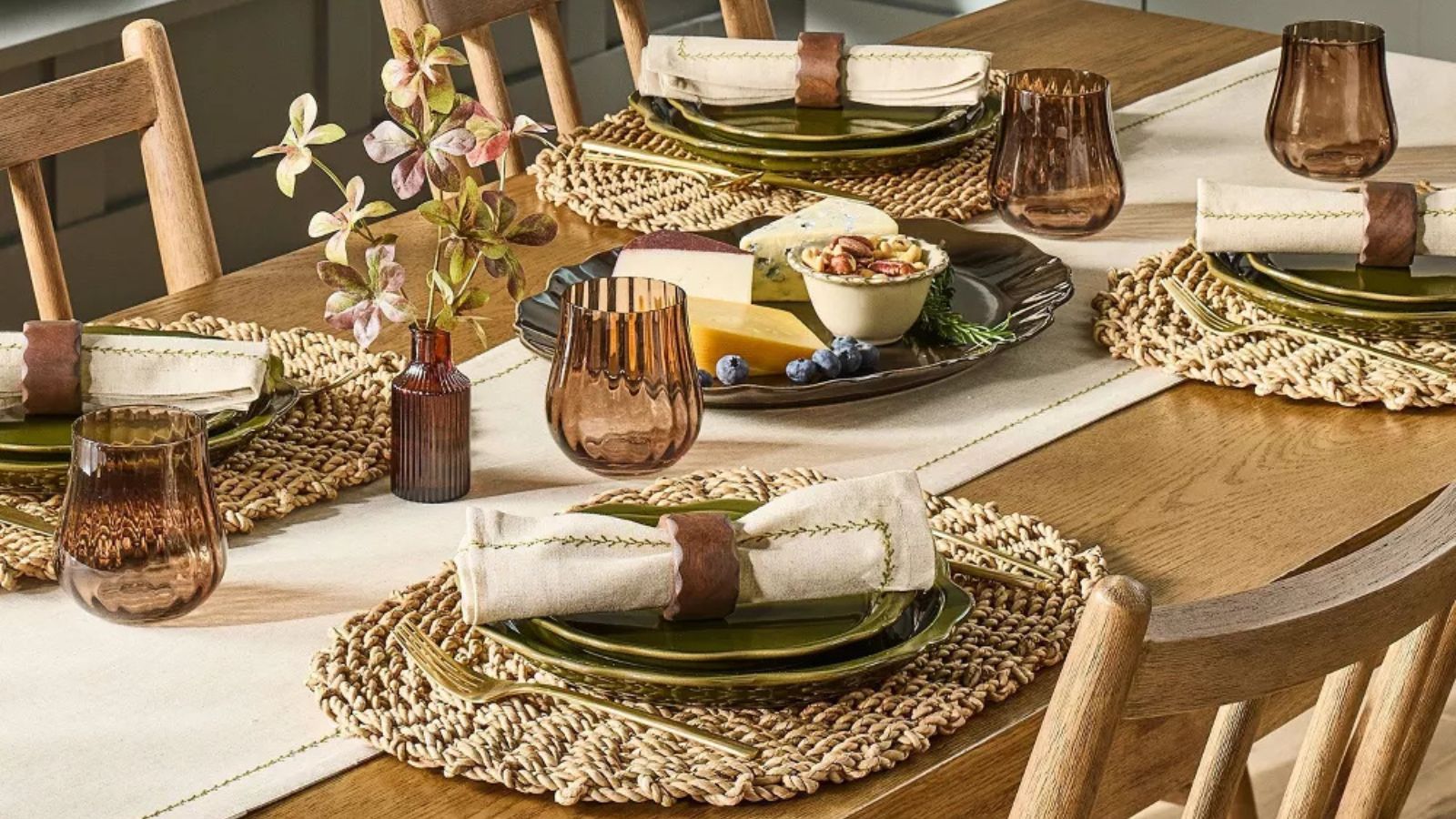 Wooden table with rattan placemats, deep green scalloped plates, cream napkins, wooden napkin rings and brown ribbed glasses