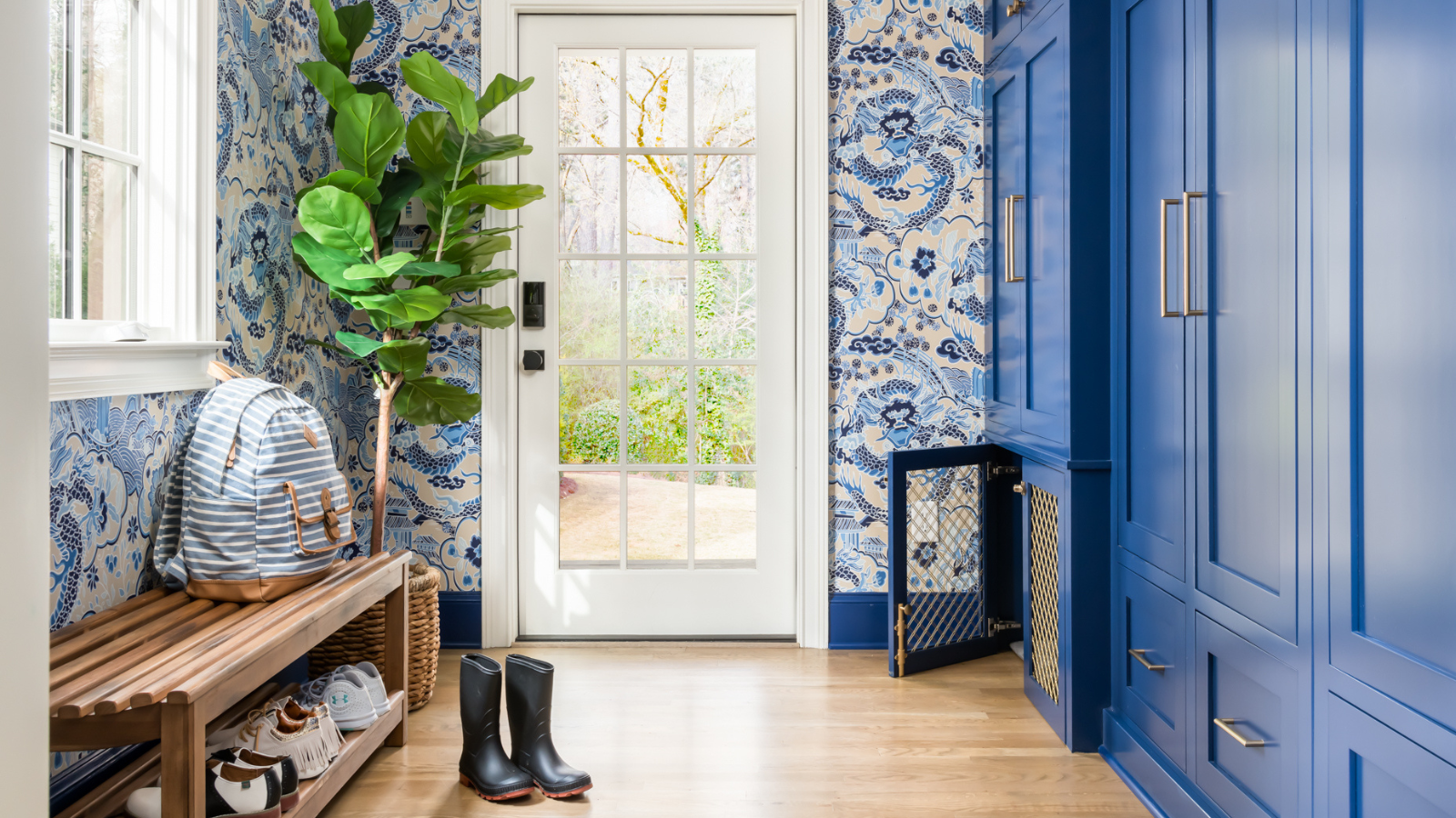 a mudroom with a vibrant blue wallpaper and blue cabinetry, a bench holding a backpack and several shoes