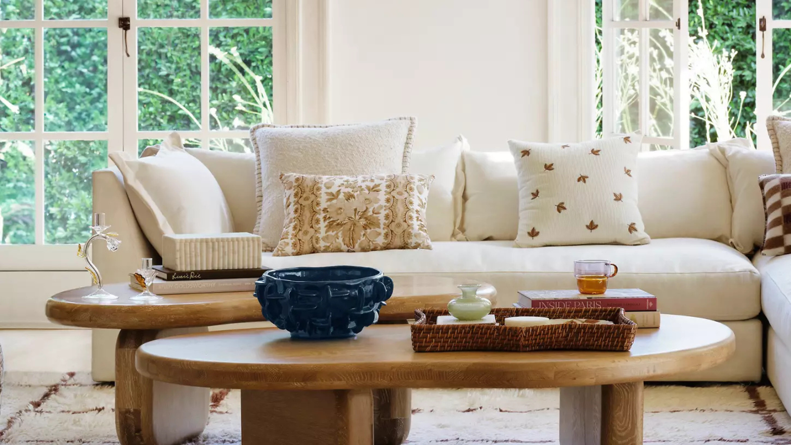 Cream living room with big arched windows, a cream corner sofa with throw pillows and two wooden coffee tables