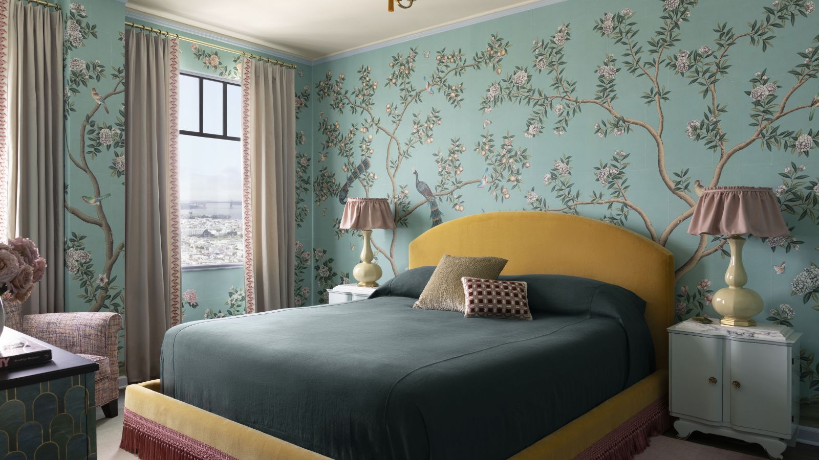 Bedroom with pale blue floral wallpaper, yellow velvet upholstered headboard and teal bedding