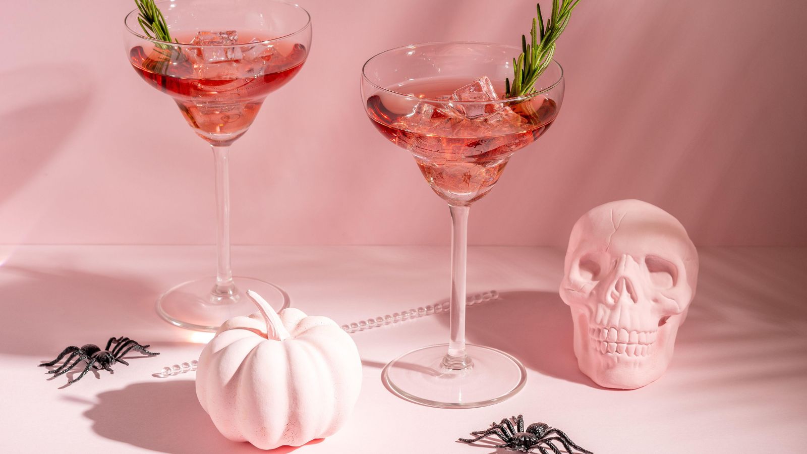 Pink cocktails against a pale pink background with pink pumpkins and skull decor below