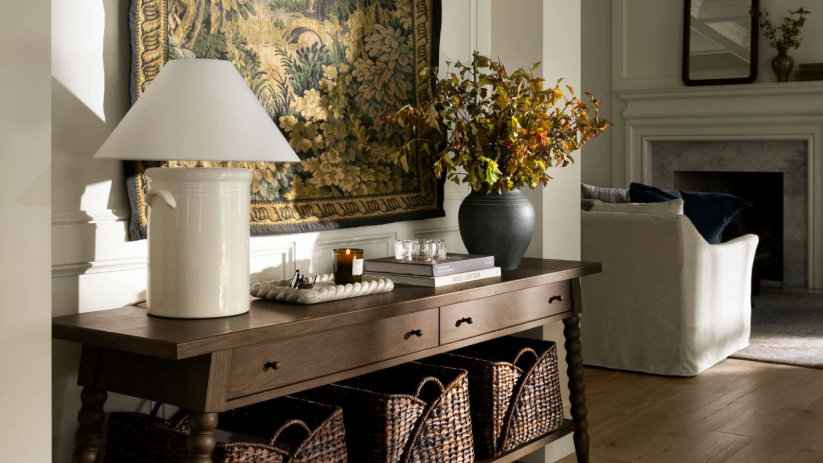 entryway table from the mcgee &amp; co fall collection styled with a bobbin vintage style console table with a tapestry hung behind and styled with baskets, a lamp and vase with foliage