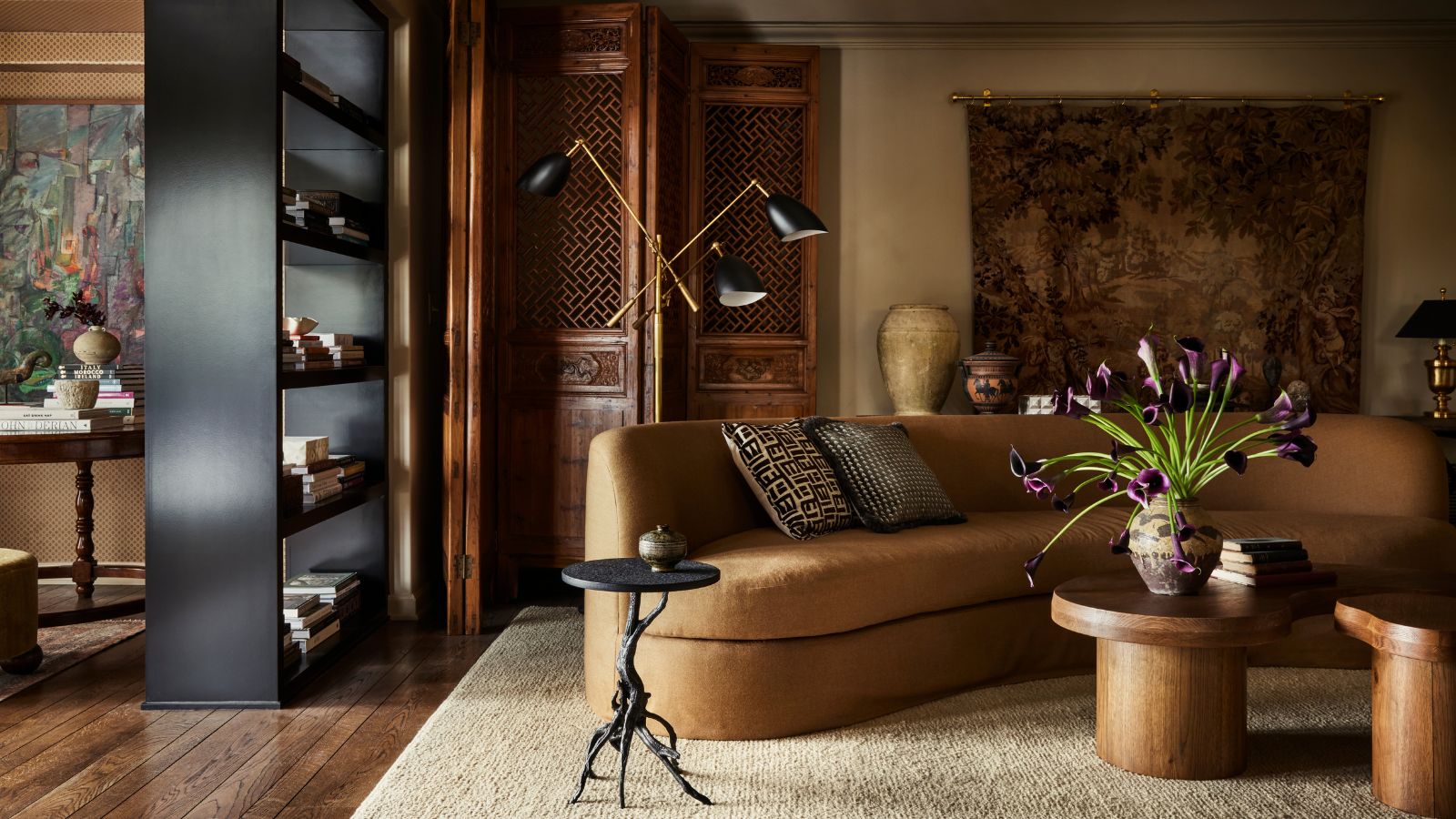 moody yet warm living room with a large camel toned curved low couch and modern black decor accents with a tapestry and original wooden carved doors