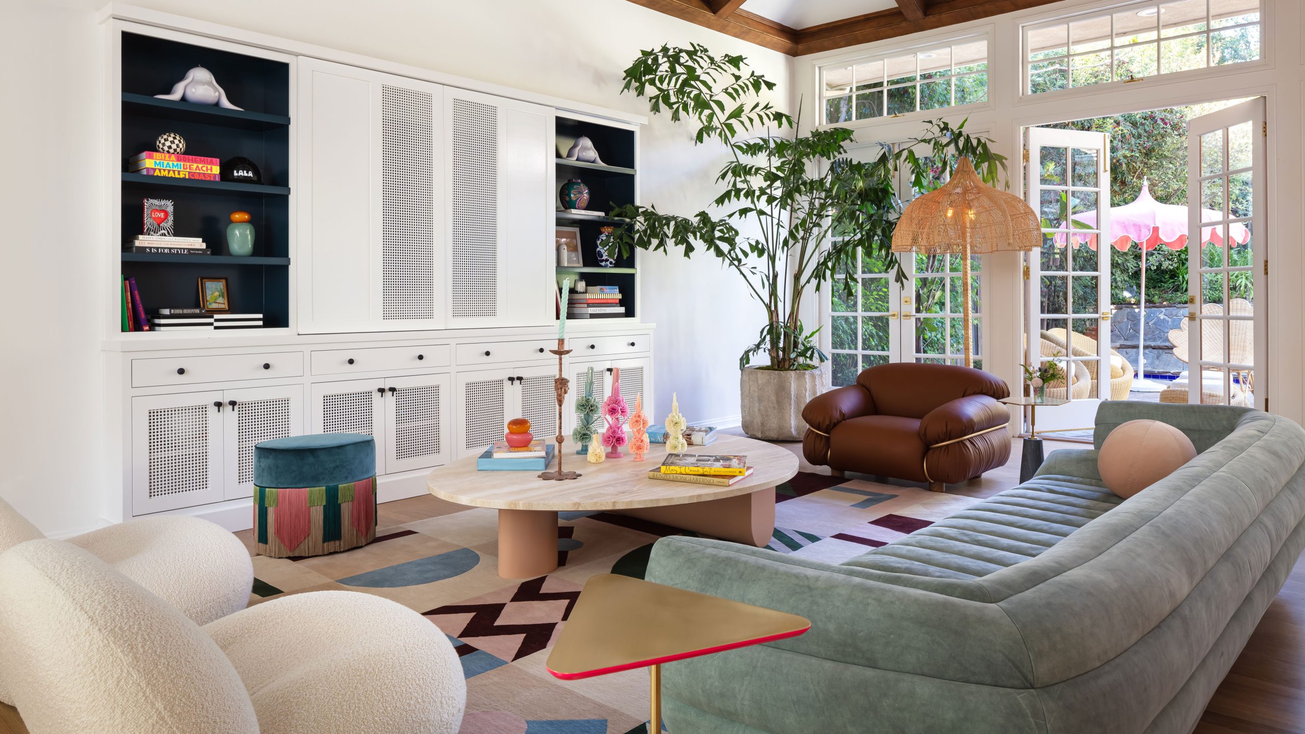 LALA Reimagined designed living room with white walls, green sofa, white armchair, round wooden coffee table, brown leather armchair and colorful rug with built-in storage