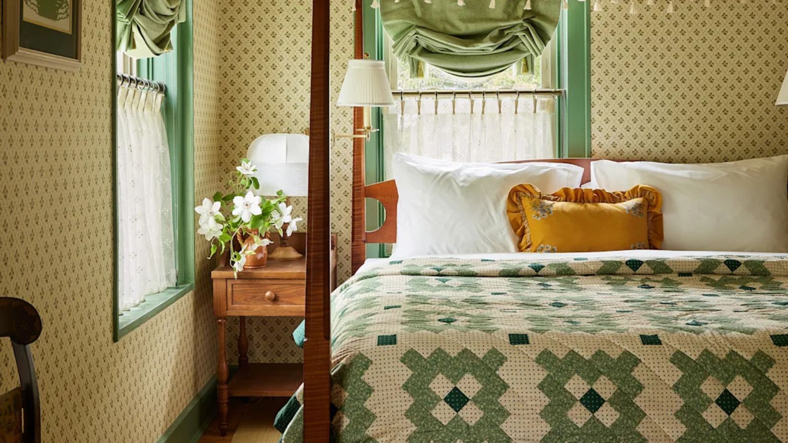 floral wallpapered hotel room with wooden four poster bed styled with bed sheets and a green patchwork scandinavian style floral quilt with a yellow ruffled pillow