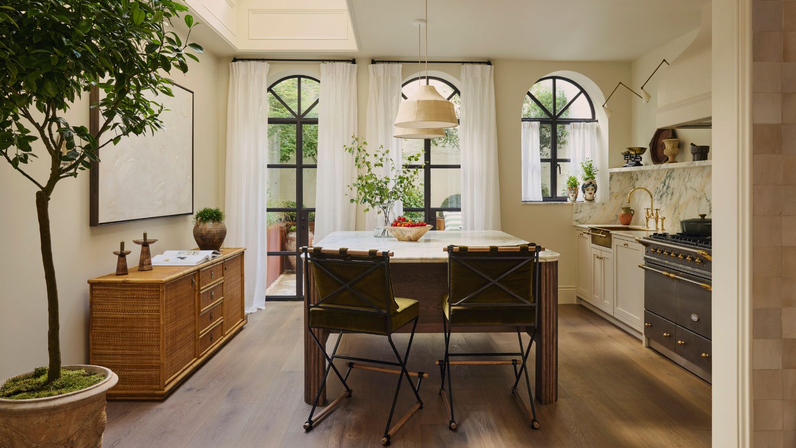 A warm neutral kitchen with a freestanding wooden island, statement marble countertops and matching backsplash, and a brass sink