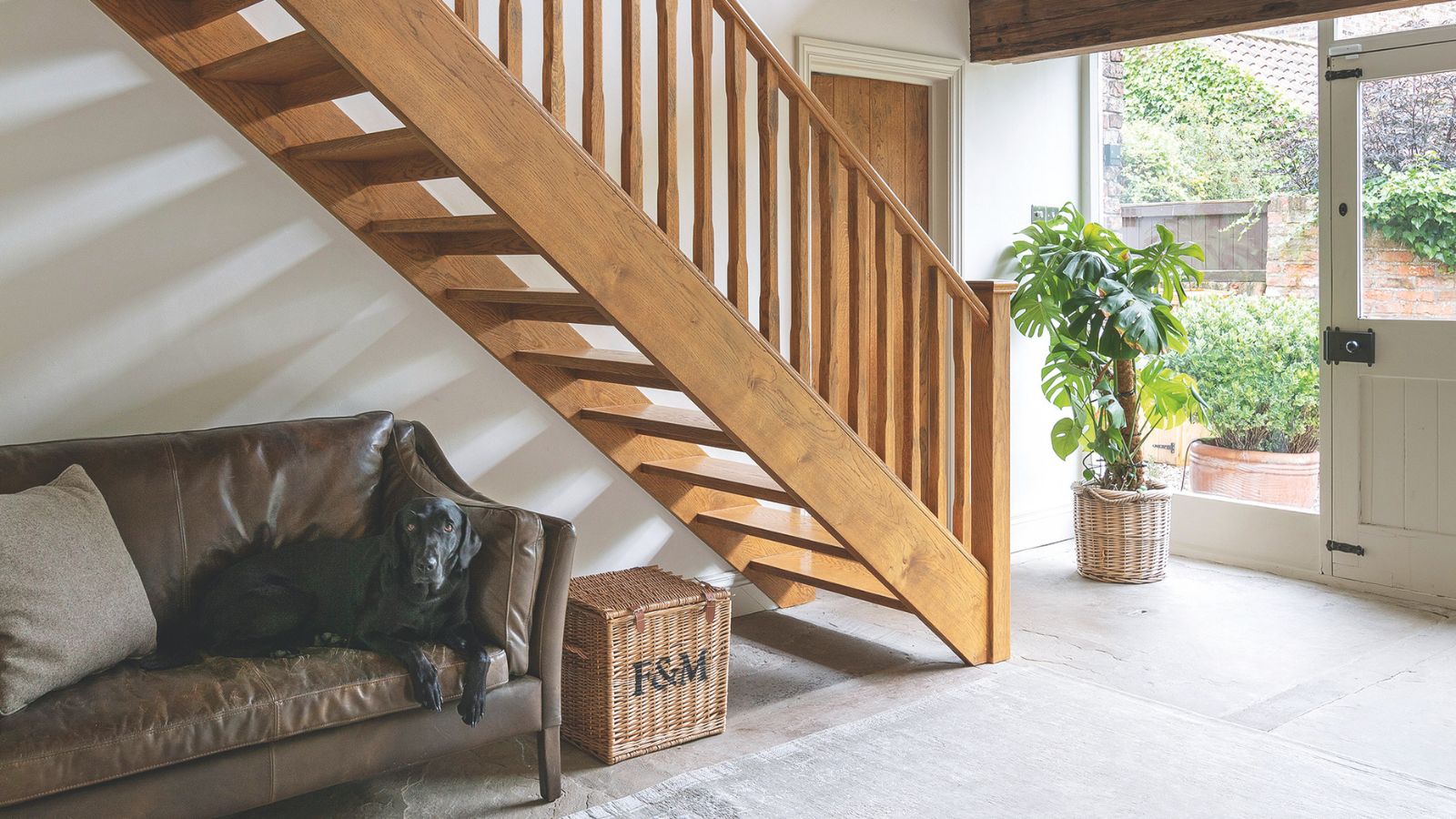 The double height stairwell in a barn conversion, a wooden staircase and banister, tiled flooring and glass windows and front door.