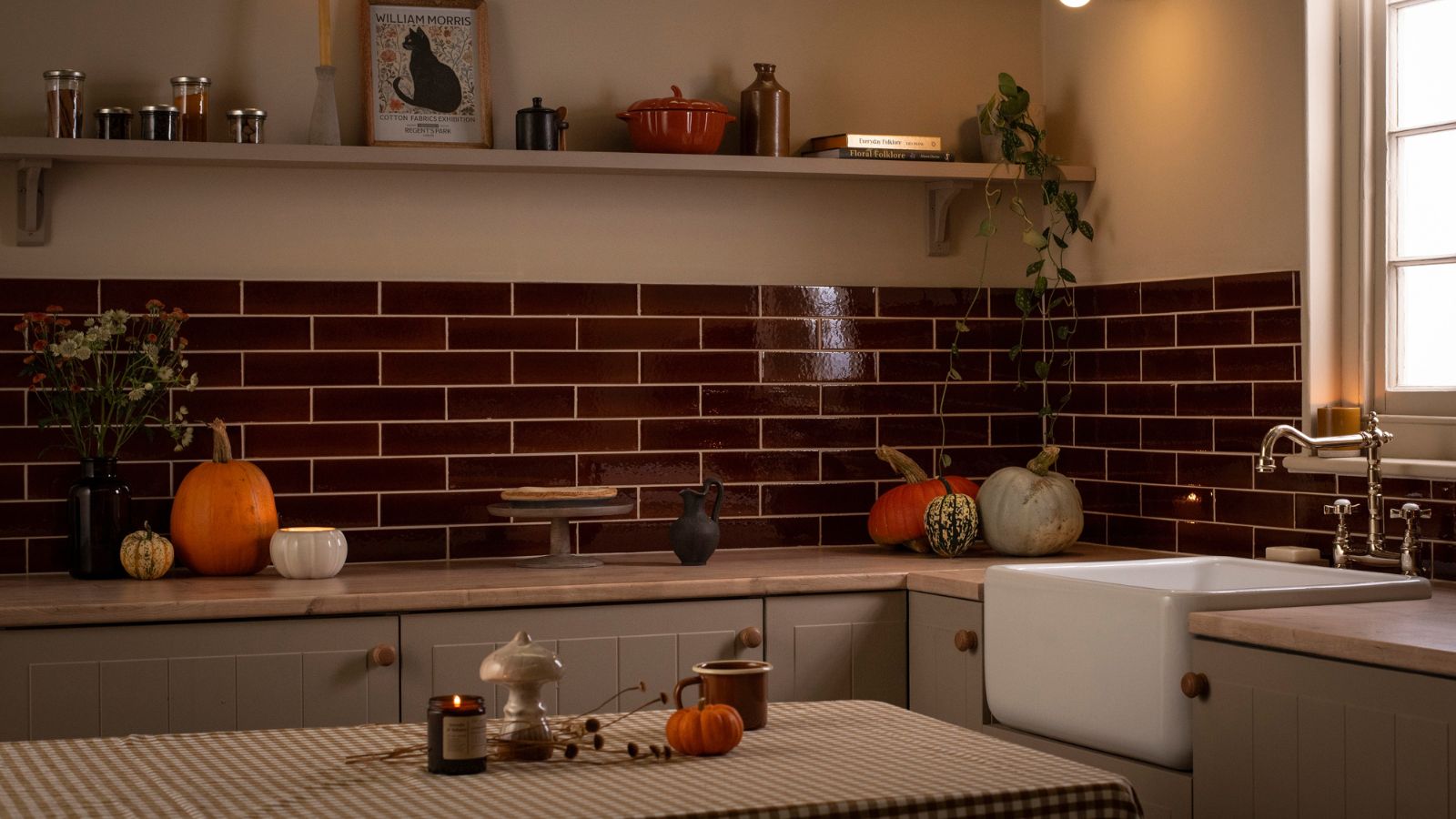 A dimly lit kitchen with deep red subway tile backsplash. Various sized pumpkins scattered on the counters.