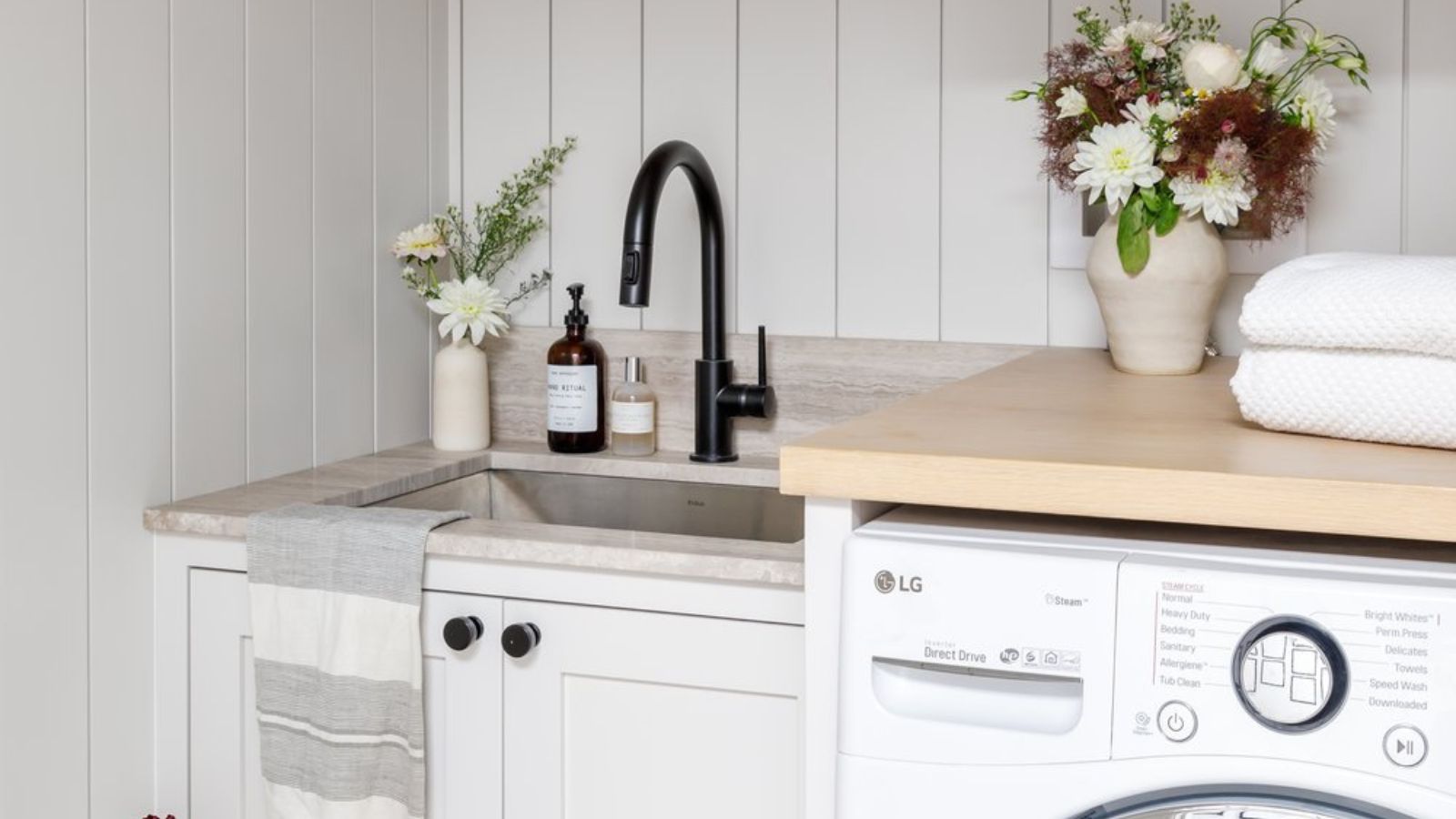 Bright neutral laundry room with styled close-up of sink, counter and top of washer
