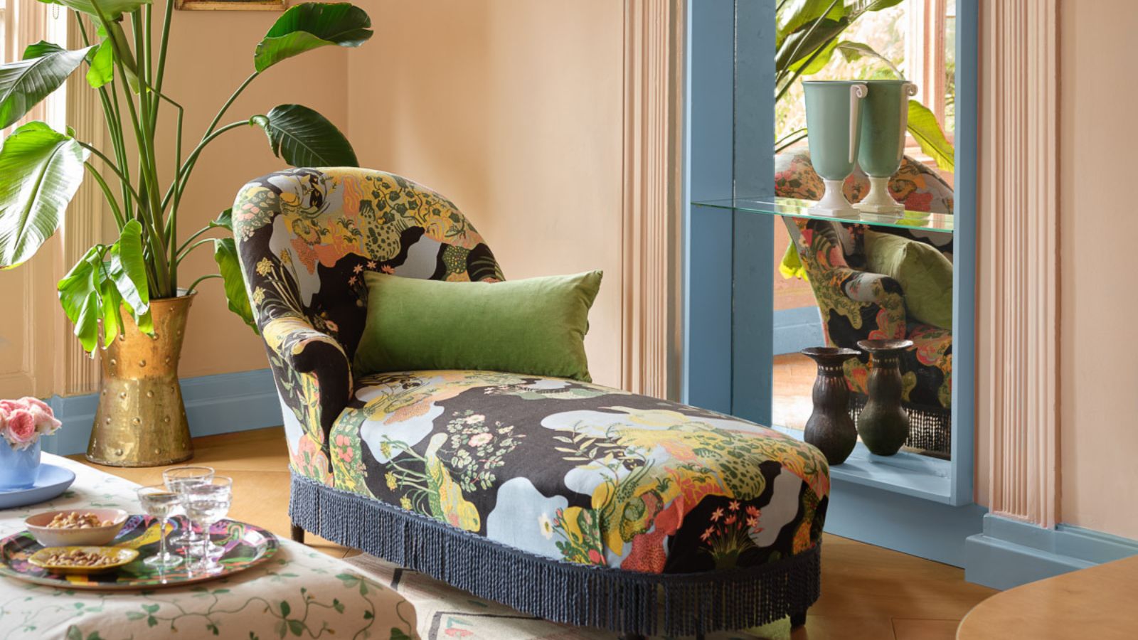 Small living room with colorful lounger and large potted plants. The walls are painted in Benjamin Moore's Desert View