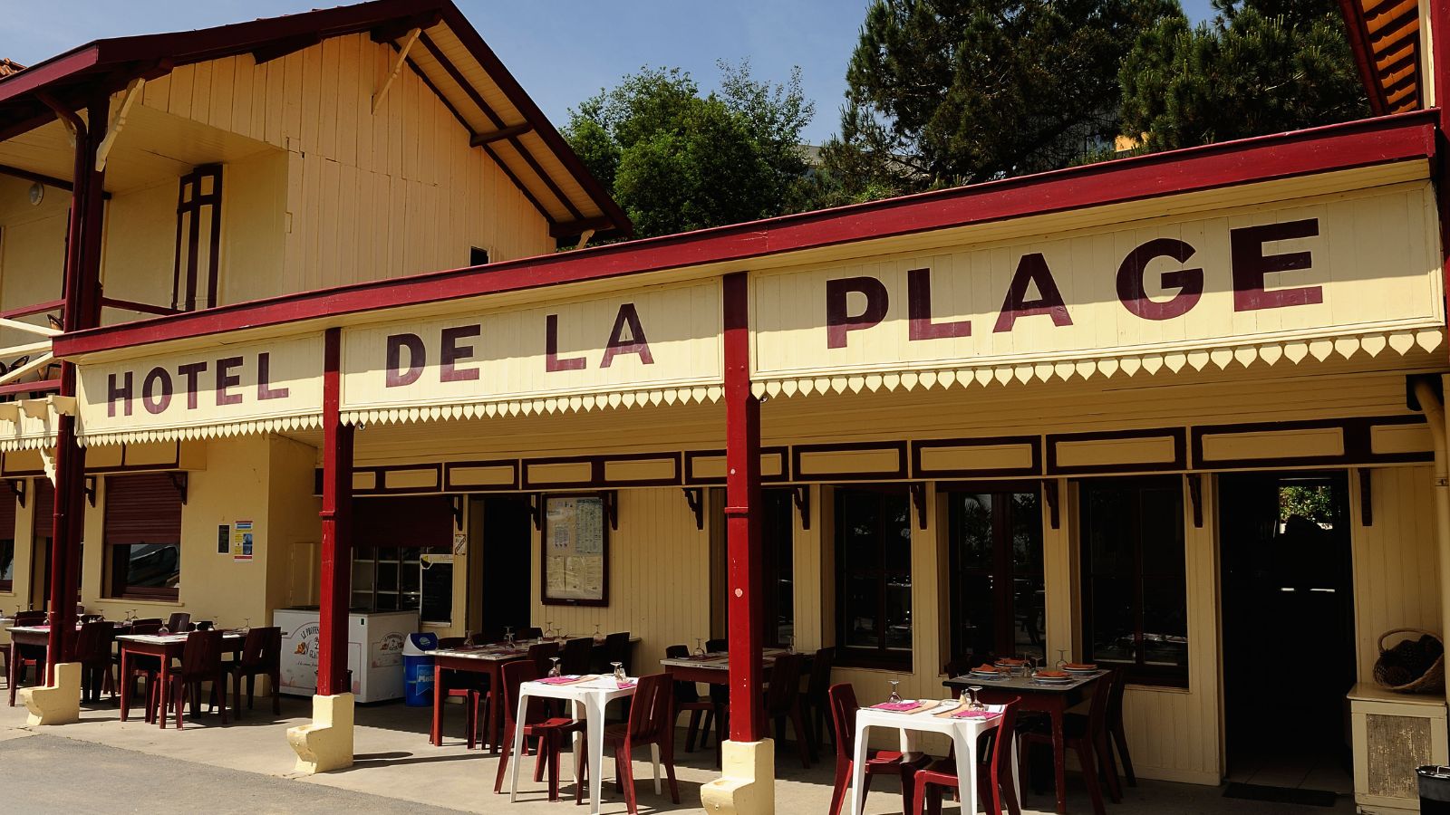 hotel de la plage in cap ferret, france with yellow and red wooden building and tables set outside