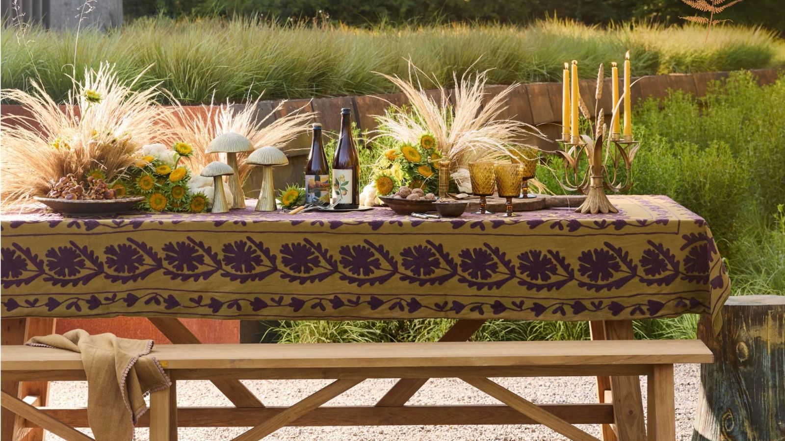 outdoor table styled for fall by Terrain with a green block print floral tablecloth styled with gold mushrooms, goblets, candles, and pampas grass and flowers