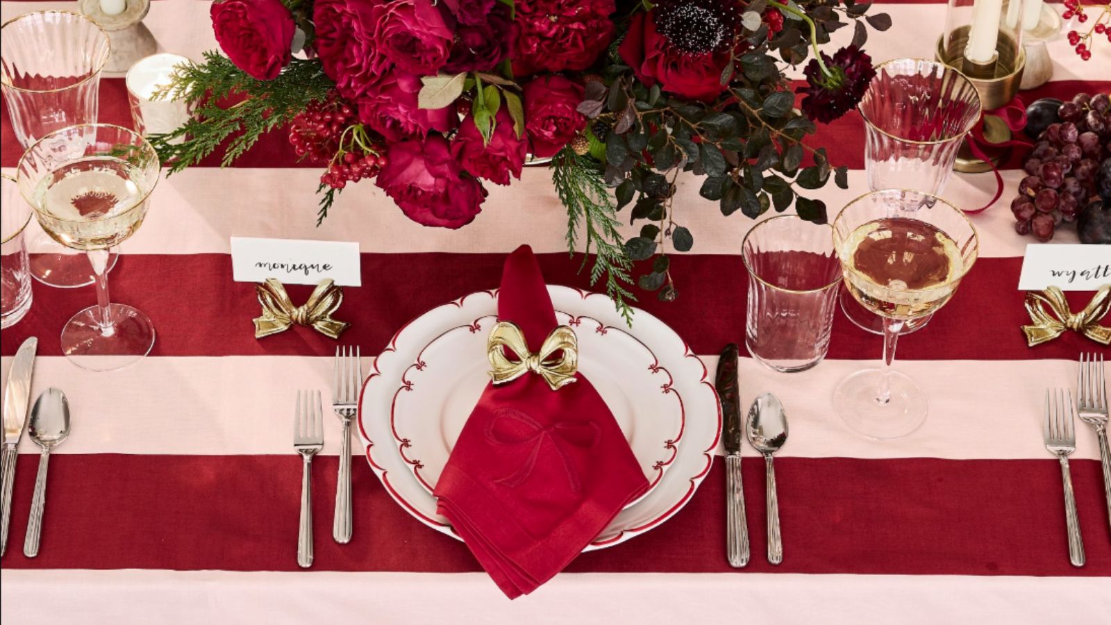Red and white themed christmas table with striped table cloth, bow napkins and place holders, red flower centerpiece and wine glasses