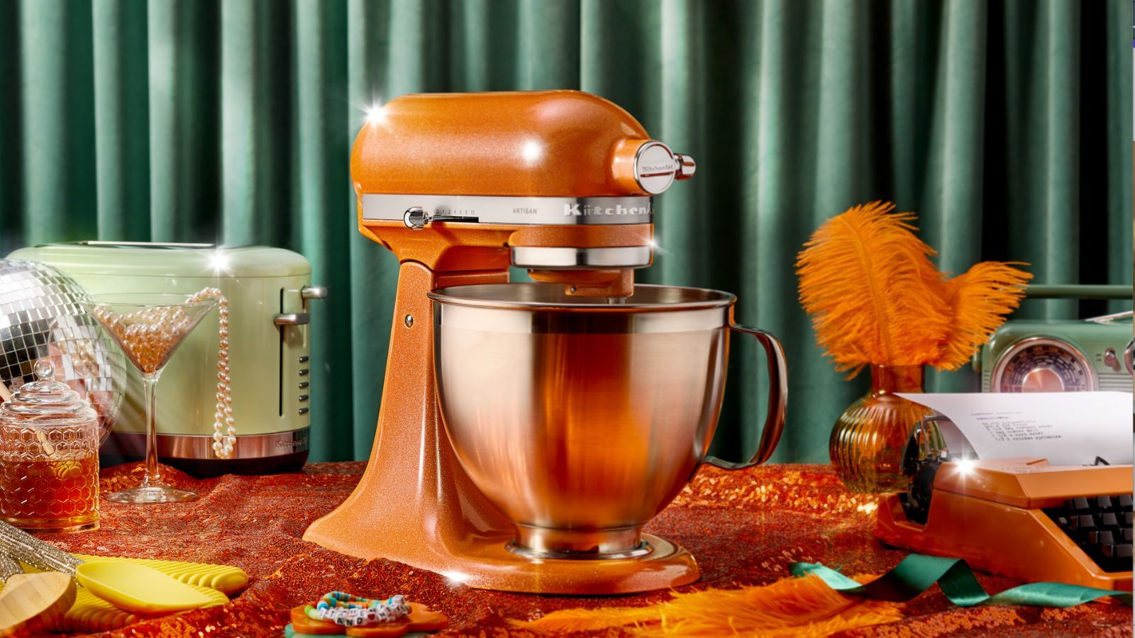 KitchenAid® Tangerine Twinkle Stand Mixer, surrounded by glamorous pearls, feathers, and disco balls