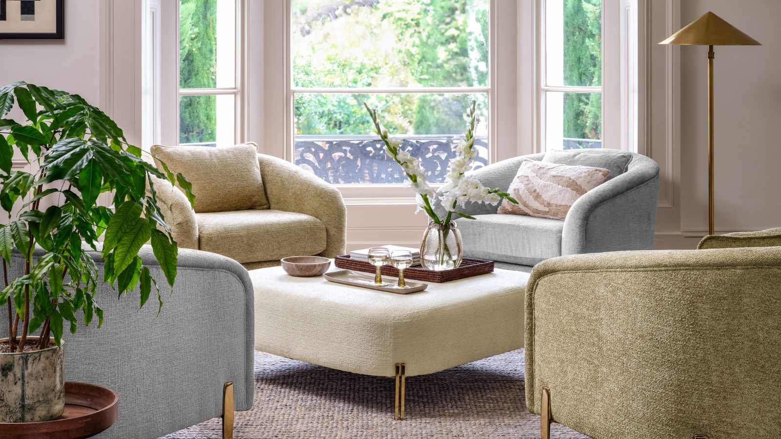 A seating nook in a white living room, with green and blue arm chairs situated around an upholstered cream ottoman.